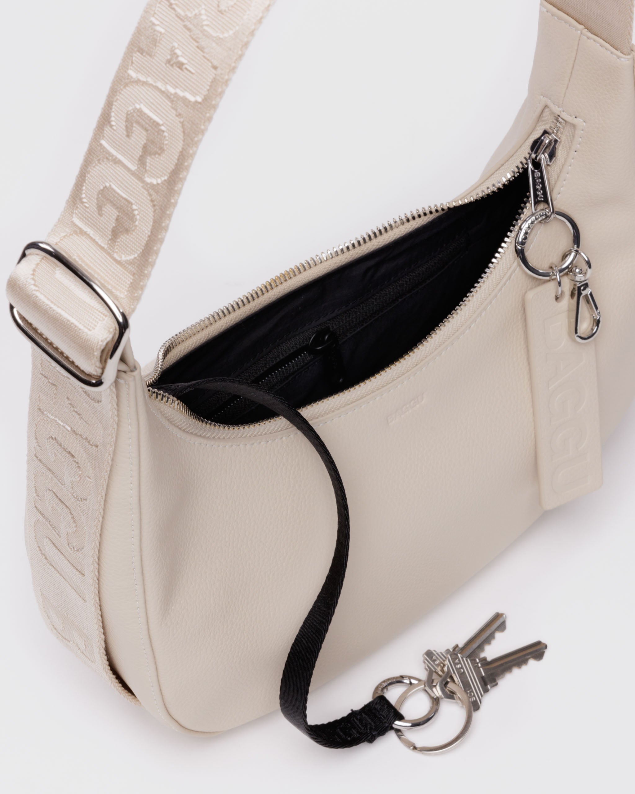 cream-small-recycled-leather-crescent-bag-strap-and-top-zip-silver-hardware-and-internal-keychain-with-keys-metal-carabiner-hanging-from-zip