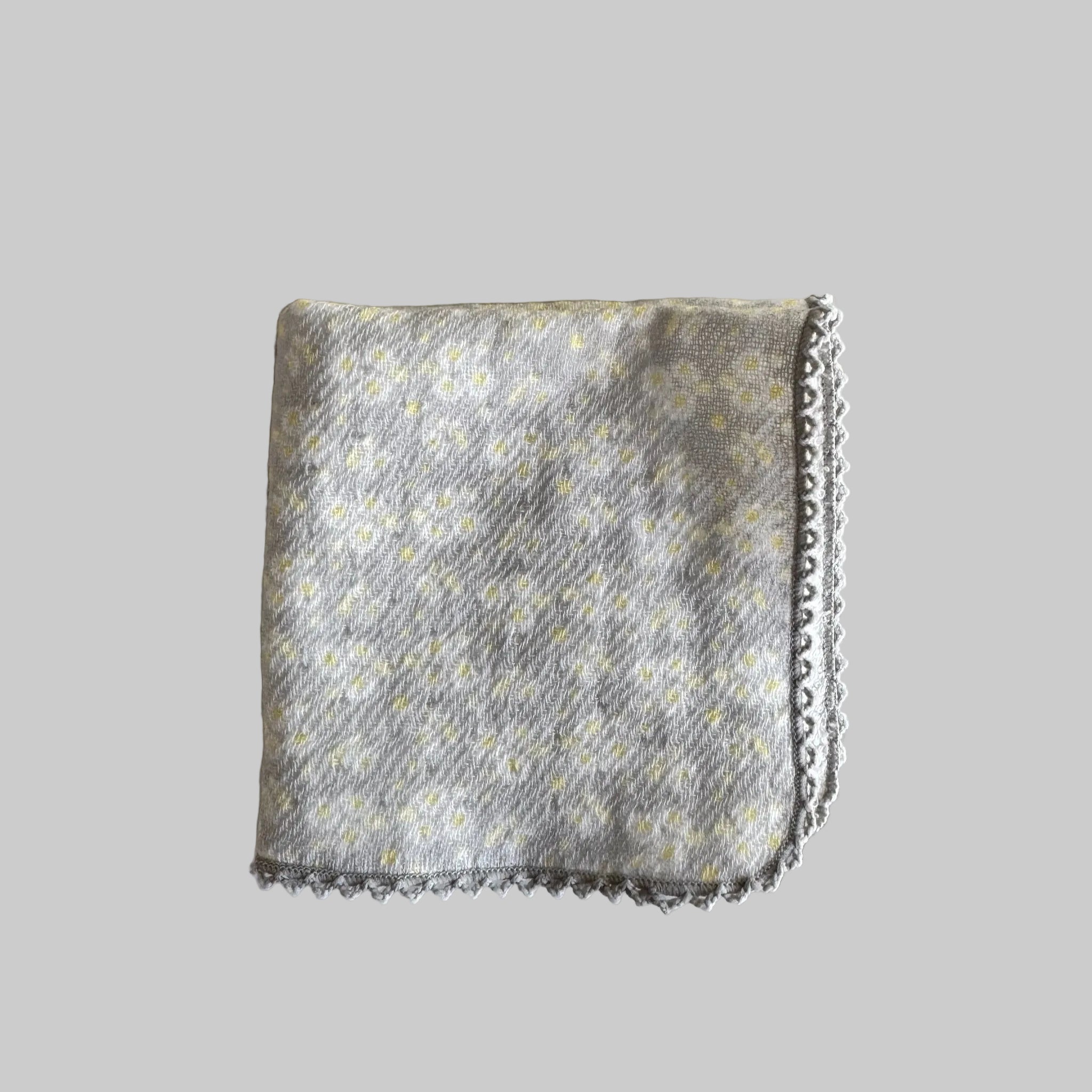 A folded grey with white and yellow flowers print and delicate grey crotchet edge face cloth.