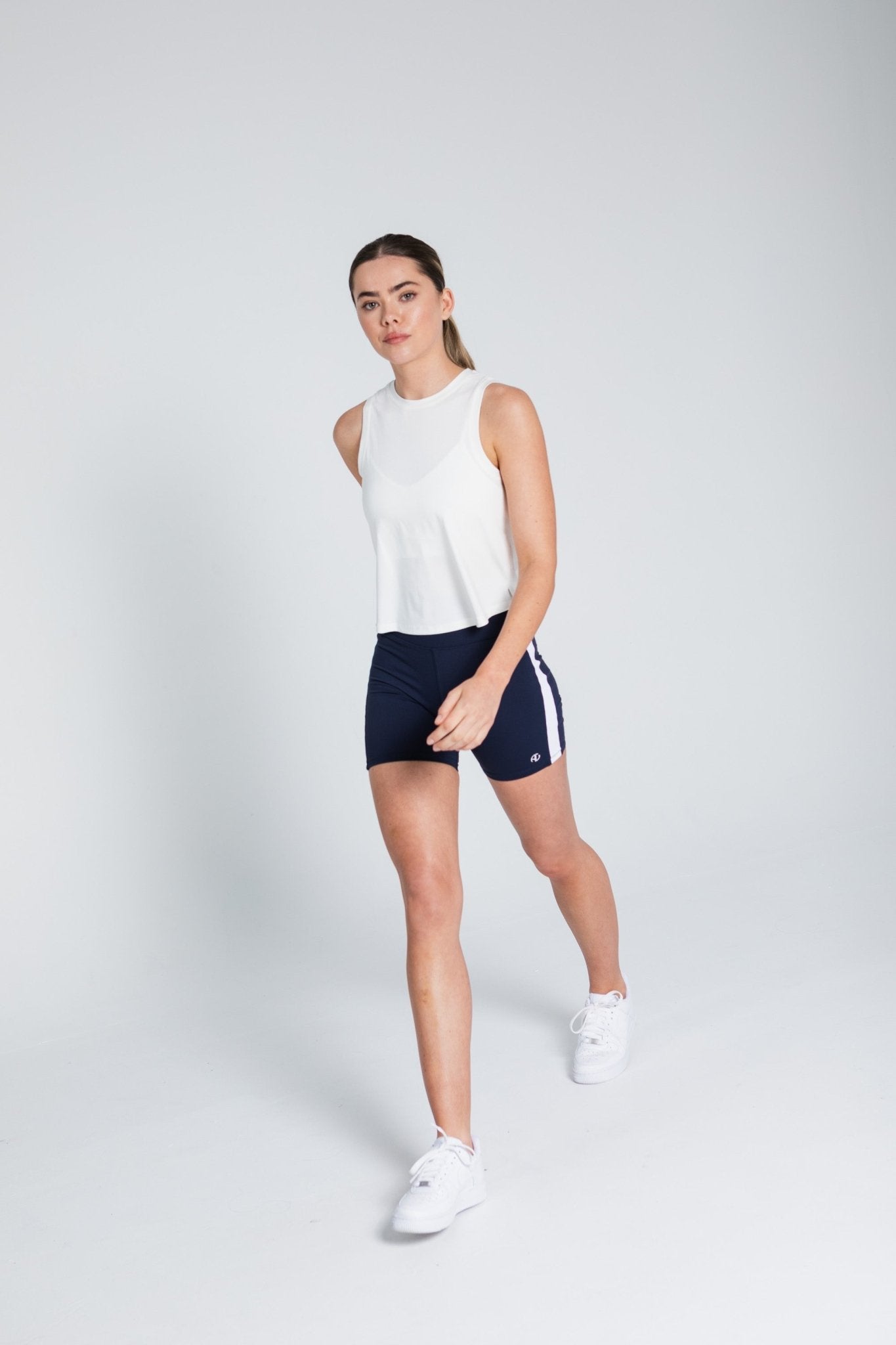 Woman walking in a white tank top and navy bike shorts with white stripe down the side.
