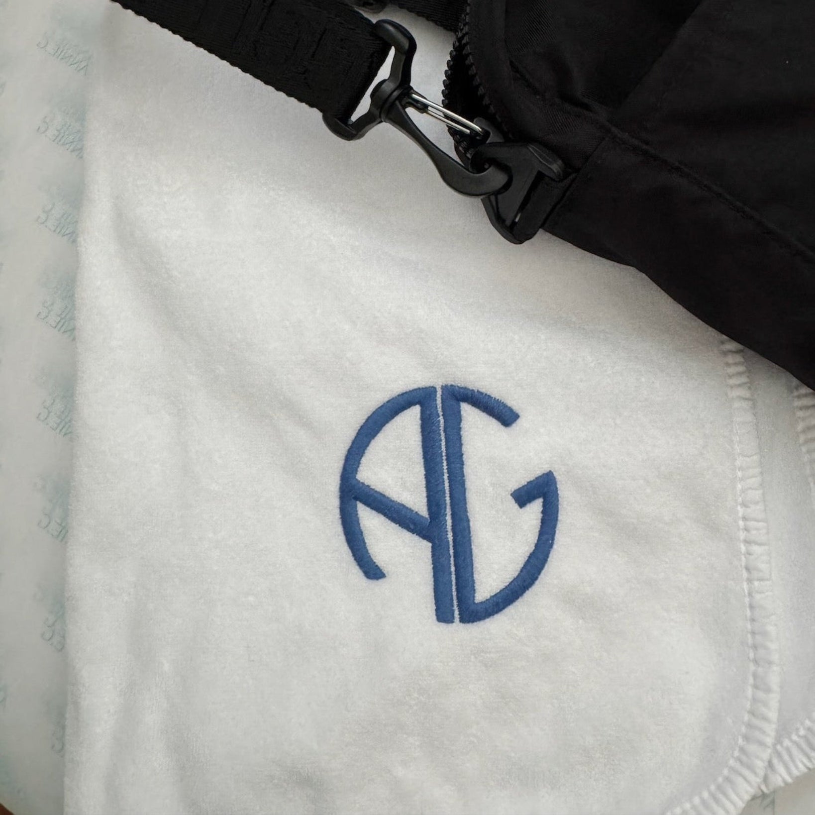 Close up of white sports towel and AG logo with black sports bag on top.