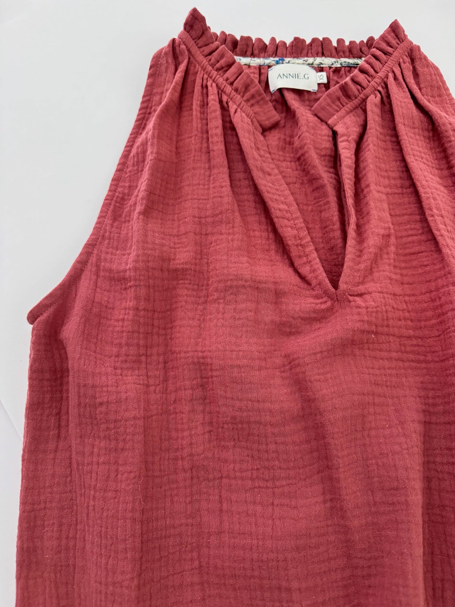 Maroon sleeveless cotton top with frill around v-neckline and floral binding inside around frill and a visible brand label