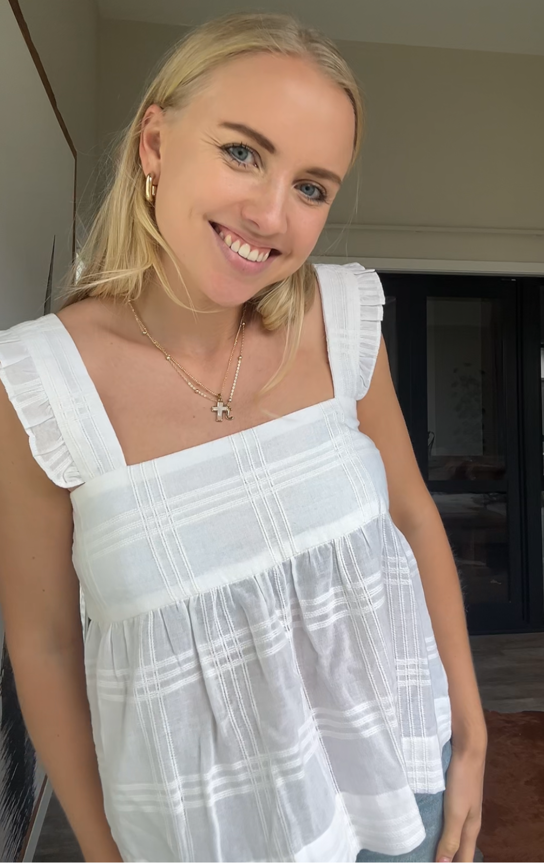 Woman wearing a white cami top with frill on strap indoors.