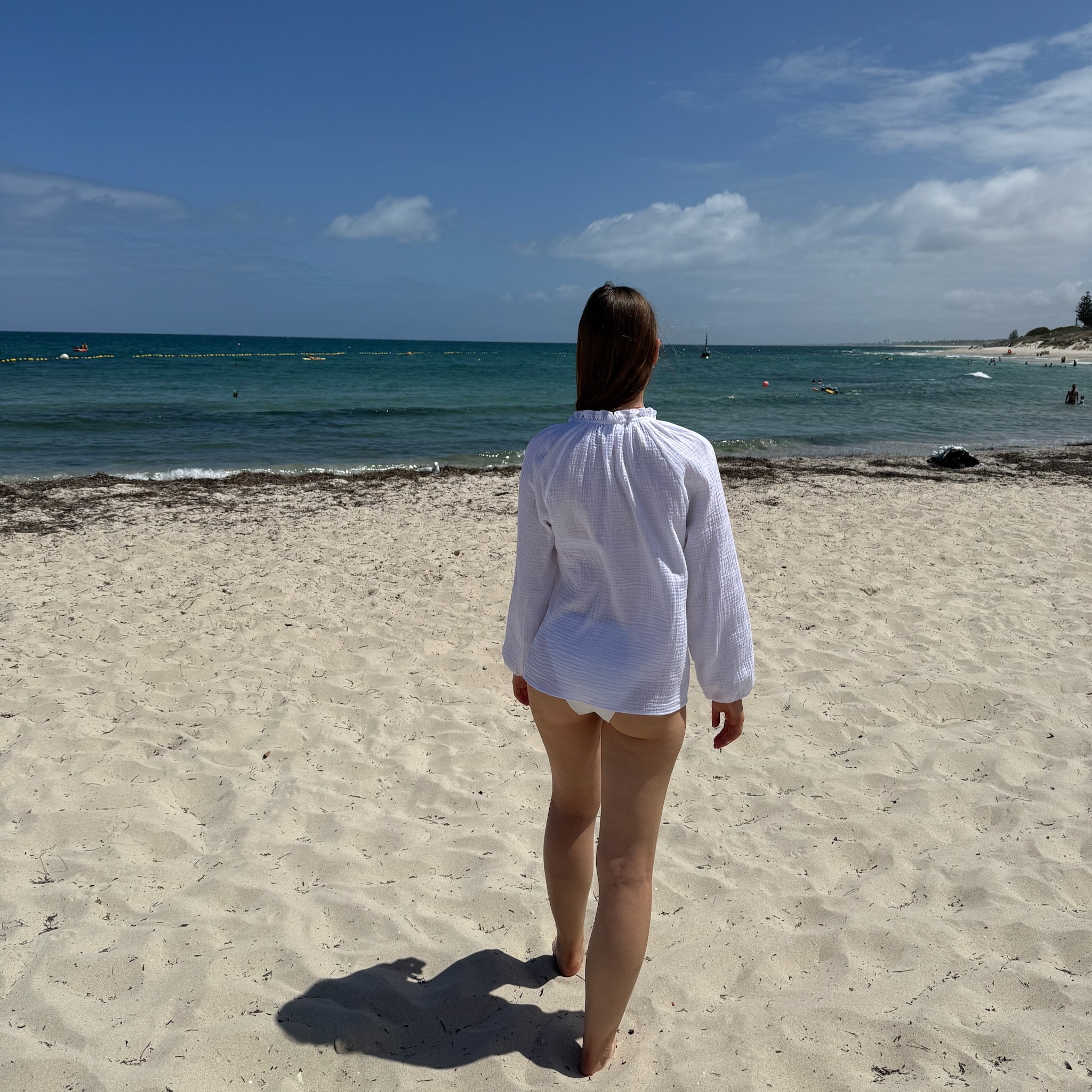 Back of a woman waering a white long sleeve top at the beach over bathers - ANNIE.G