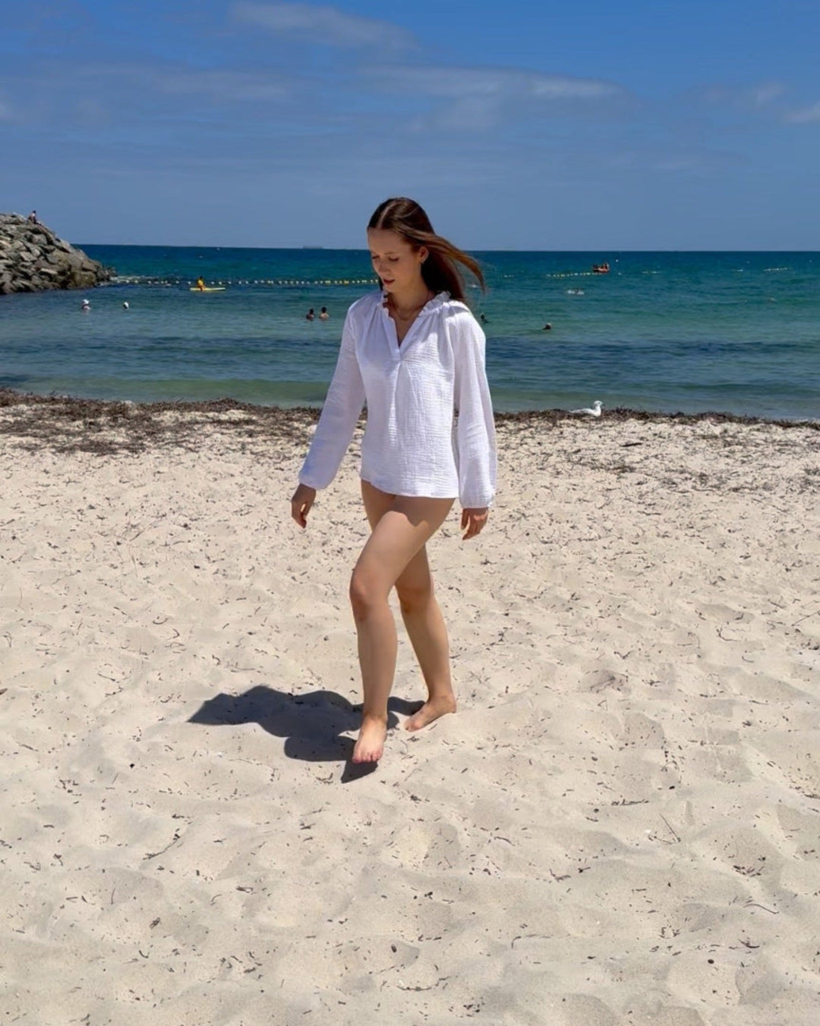 Woman wearing a white long sleeve cotton top waling on a beach - ANNIE.G