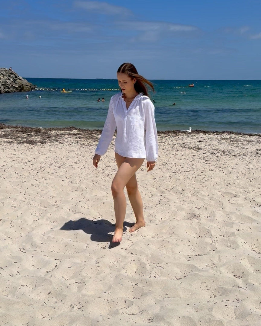 Woman wearing a white long sleeve cotton top waling on a beach - ANNIE.G