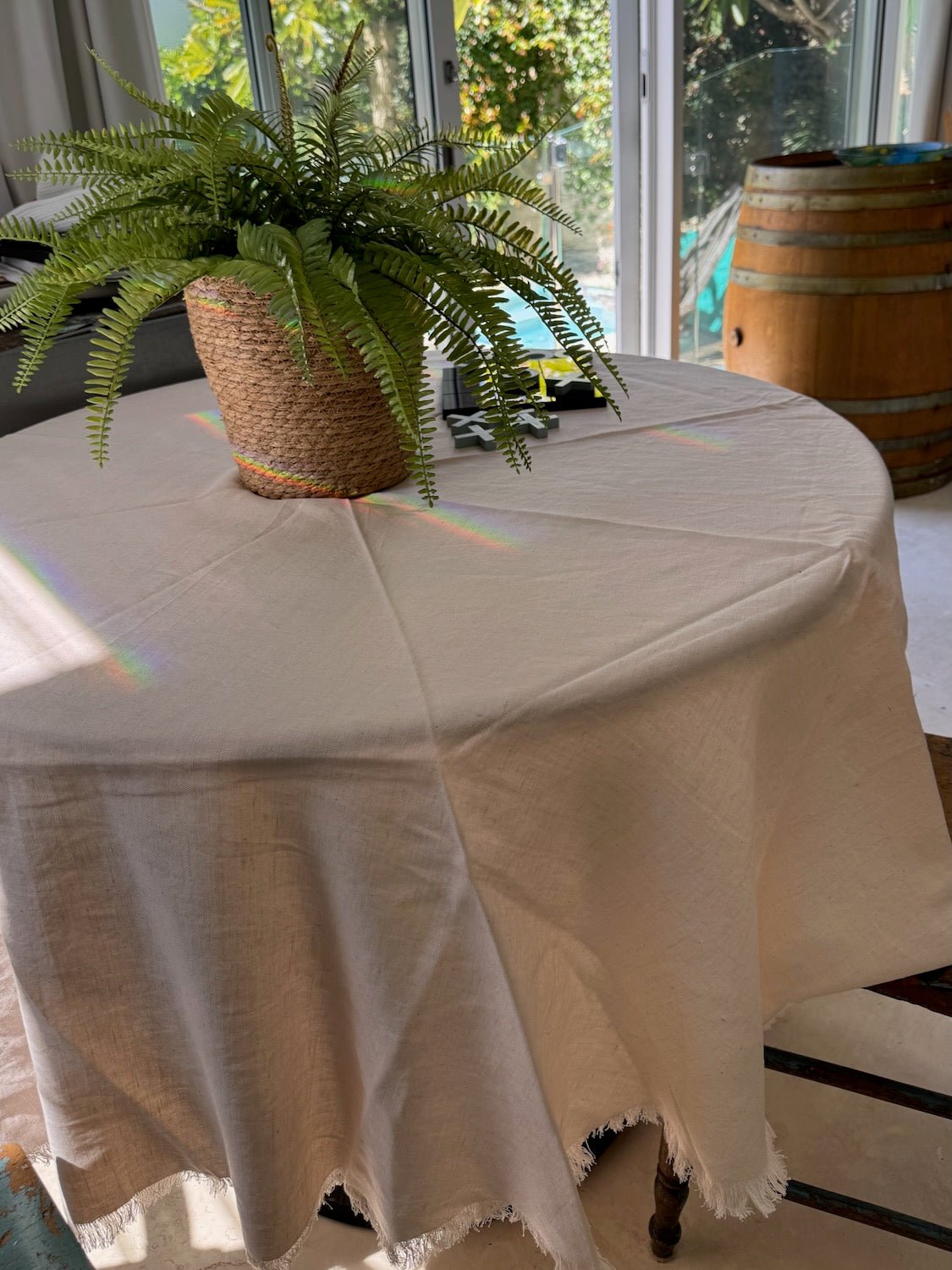 Round table with a blush pink tablecloth and a potted plant in a room with large windows.