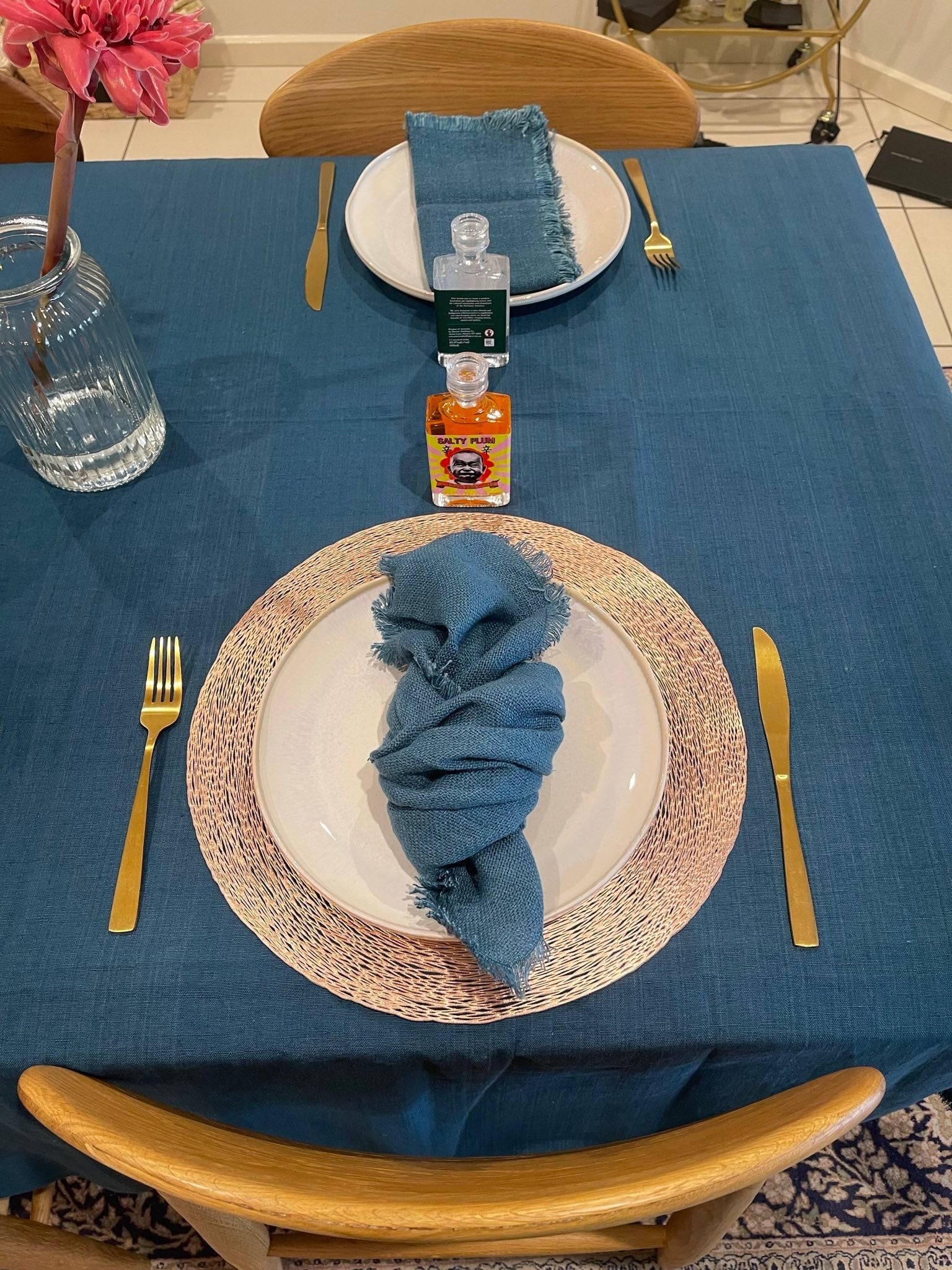 Dining table setting with teal tablecloth and napkins, gold cutlery, and bottles.