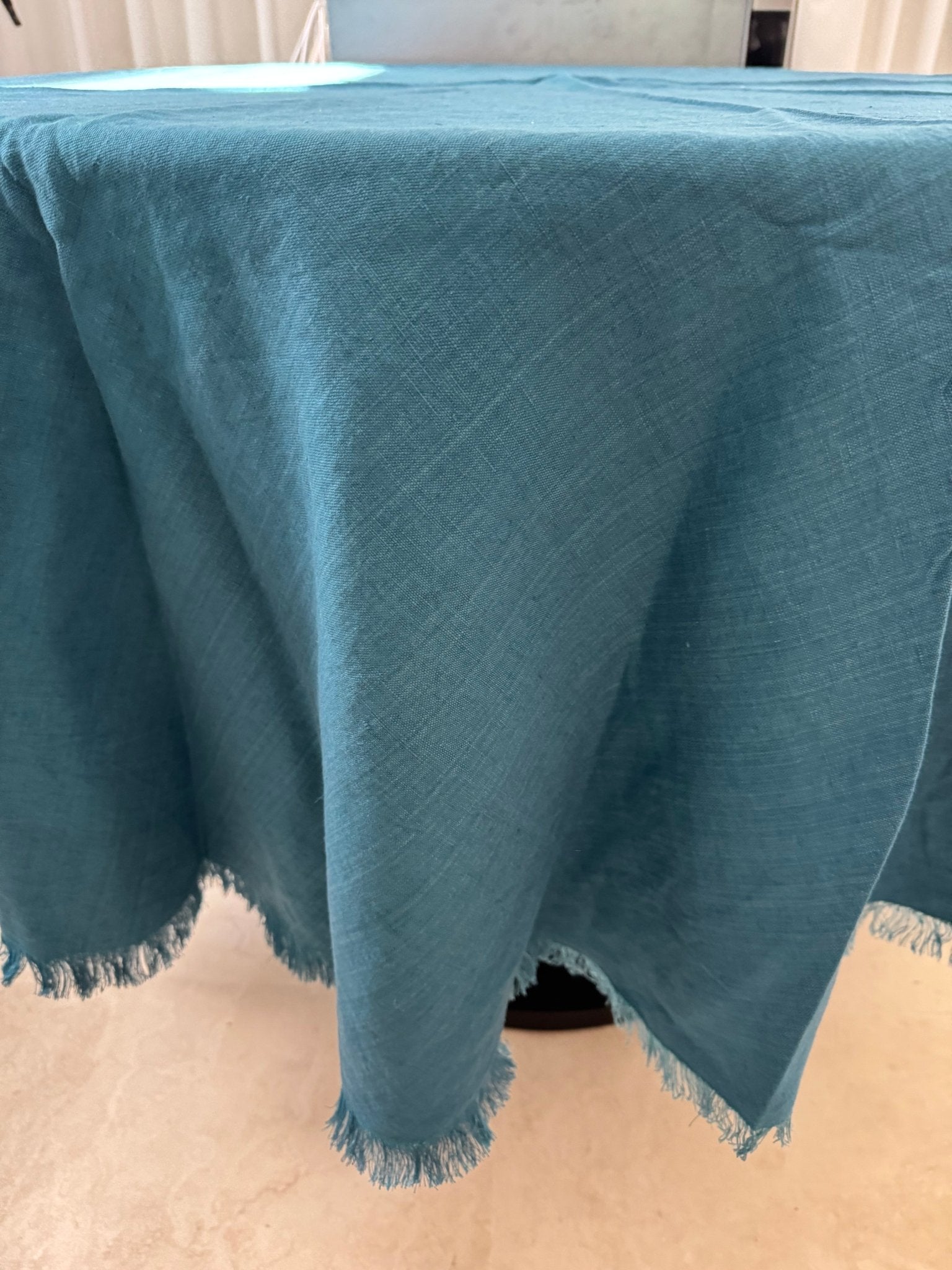 Teal round tablecloth with frayed edges on a round pedestal table