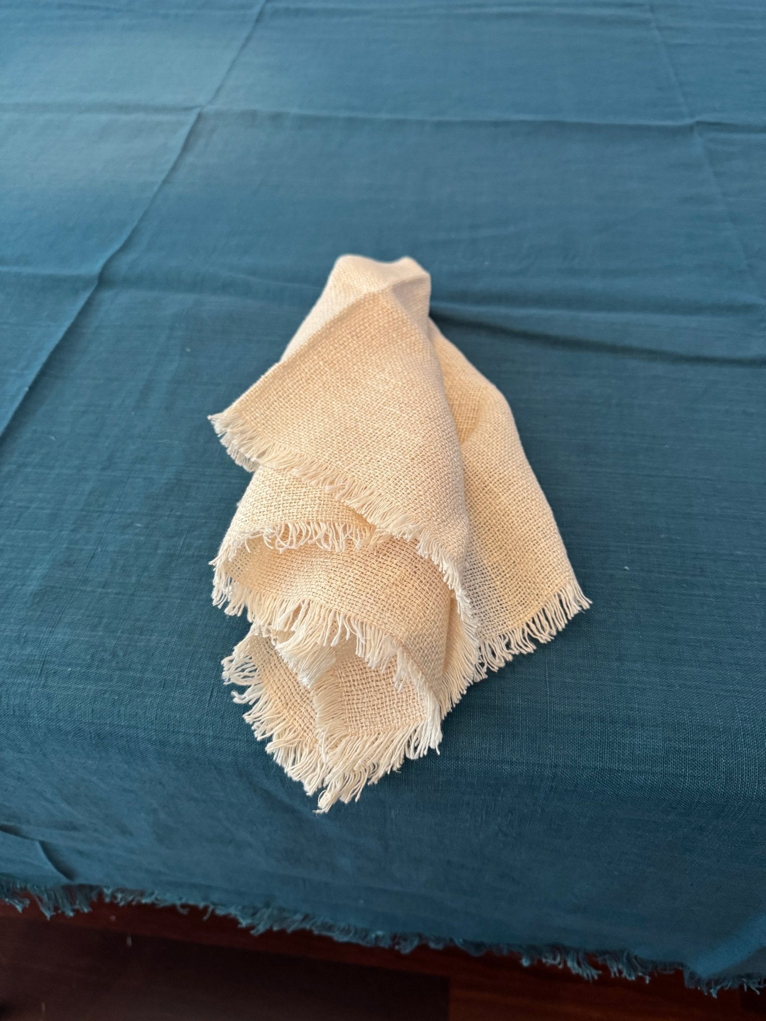 Teal tablecloth with fringe edge and blush napkin laid on top