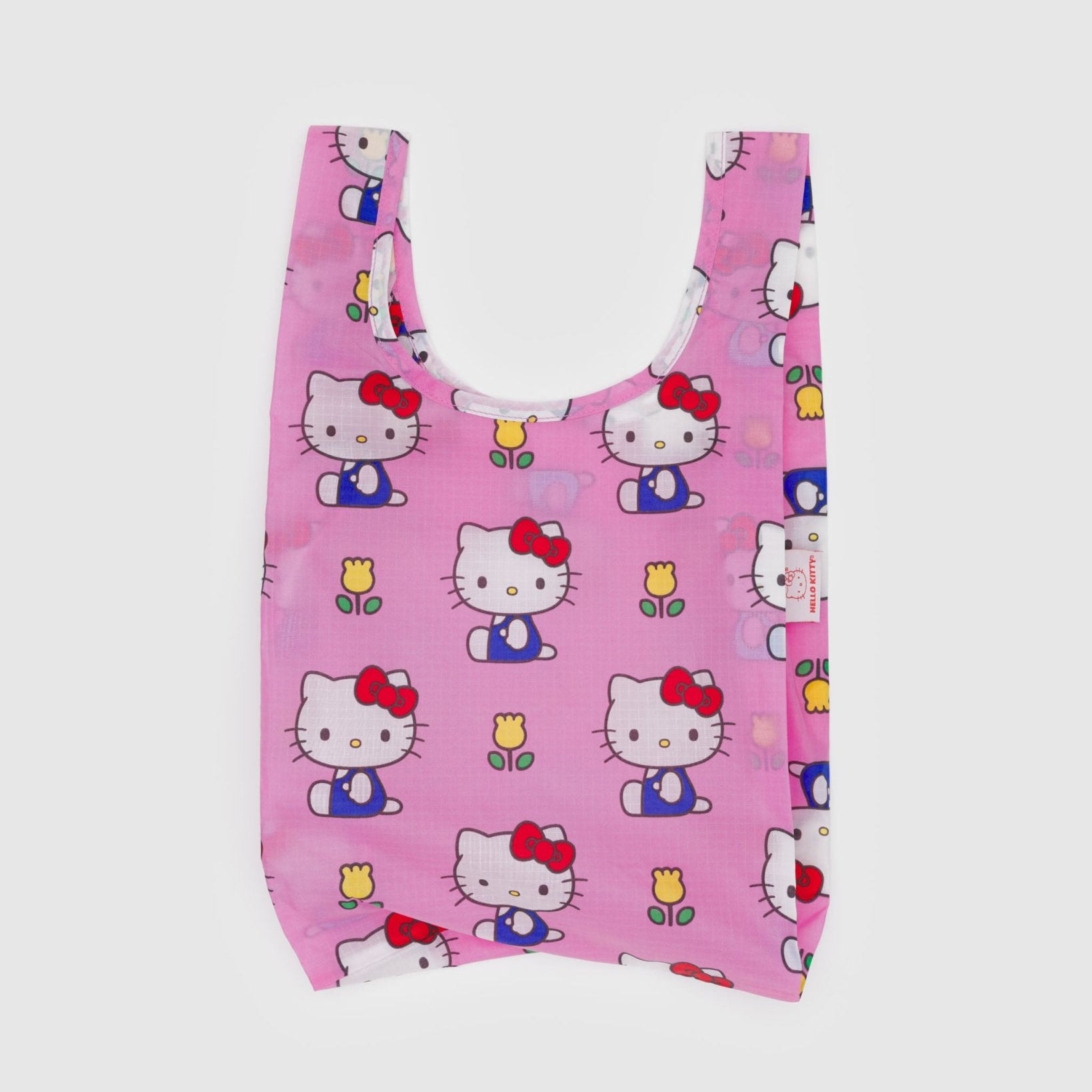 Pink reusable bag with print of a white cat wearing blue overalls with red bow near ear and yellow tulips