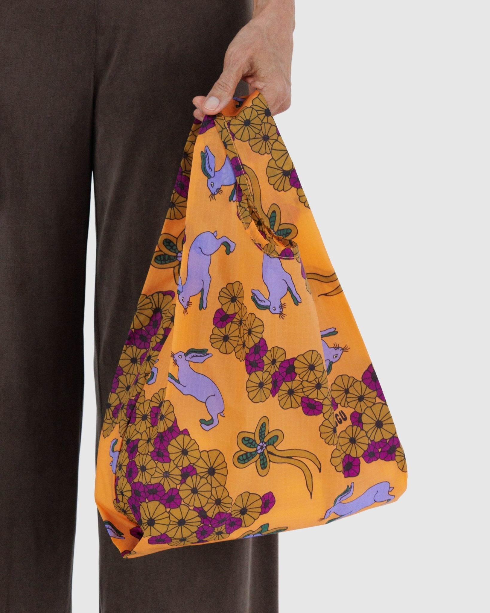 Person holding a colourful orange reusable baby size bag with purple rabbit and floral pattern 