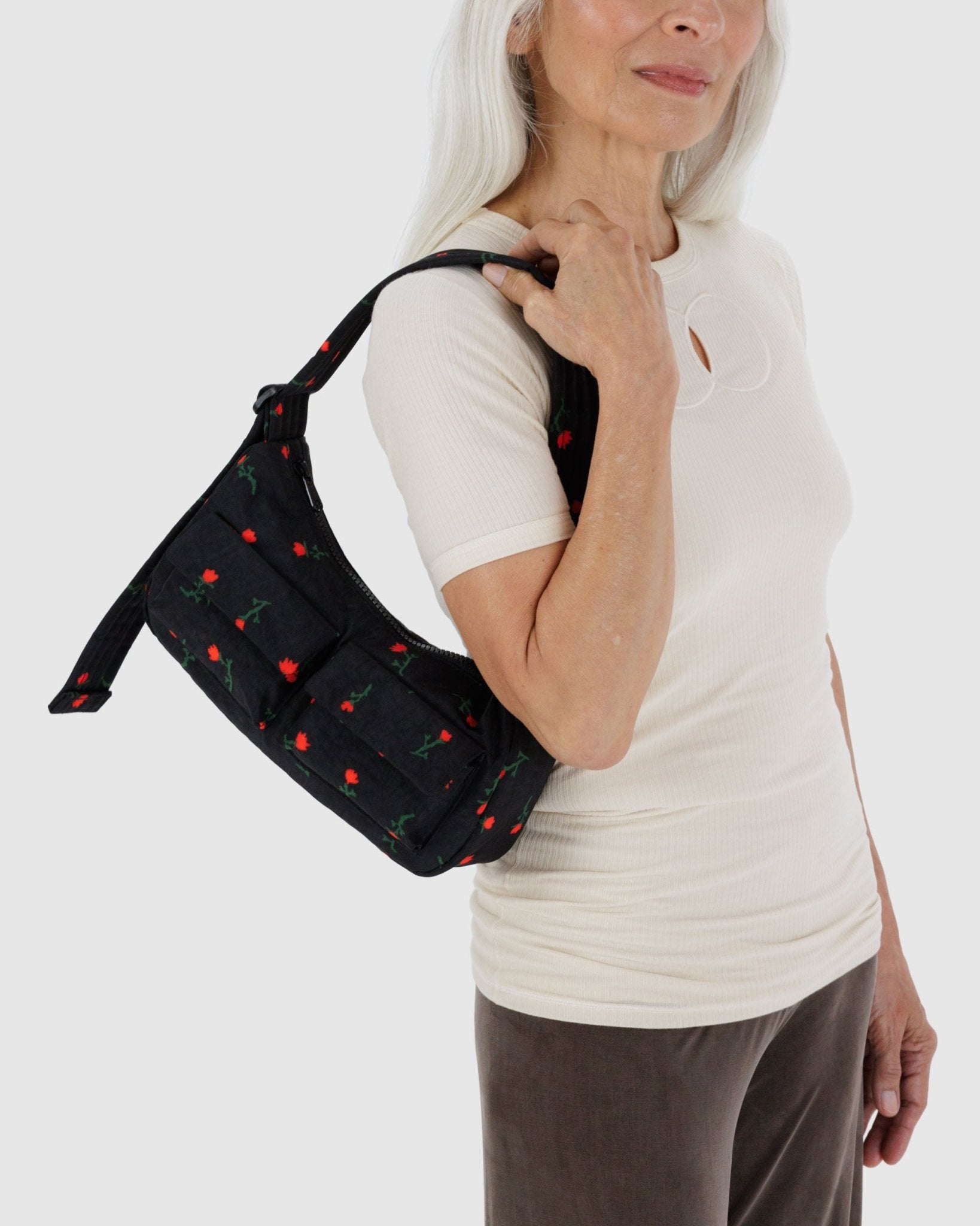 Woman holding a small black cargo shoulder bag with red wildflower pattern on shoulder, front cargo pockets and adjustable strap