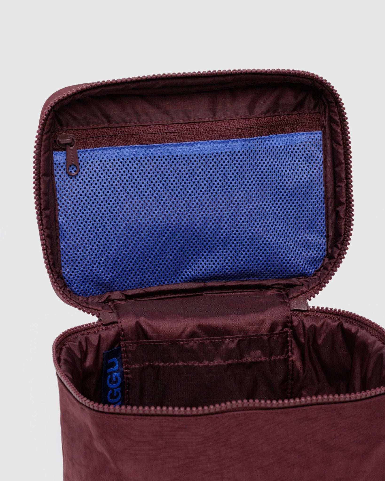 Open maroon large cosmetic case with one main compartment and blue mesh zip pocket inside lid 