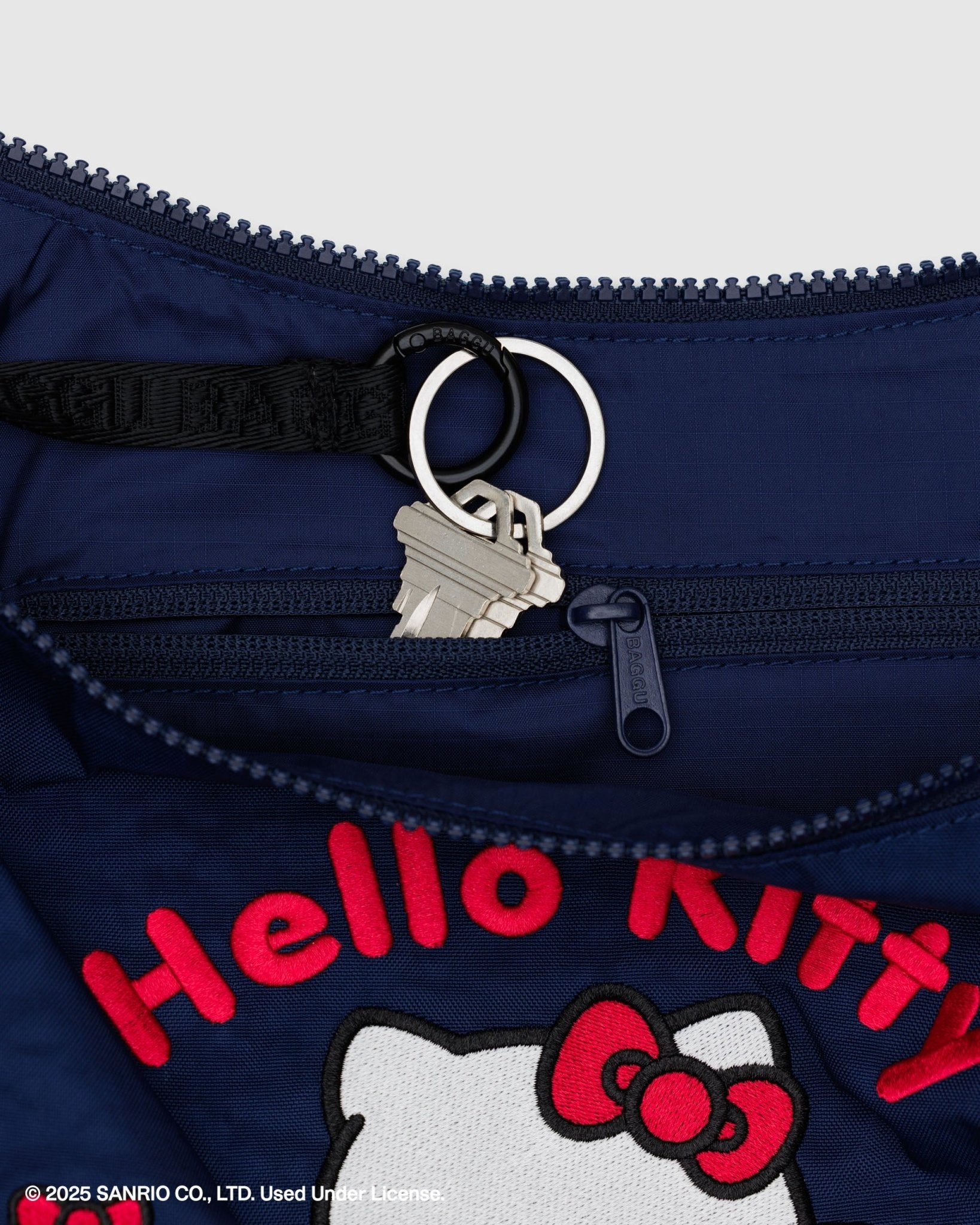 Navy blue bag with red 'Hello Kitty' embroidery branding and character on front and a keychain going into zip pouch