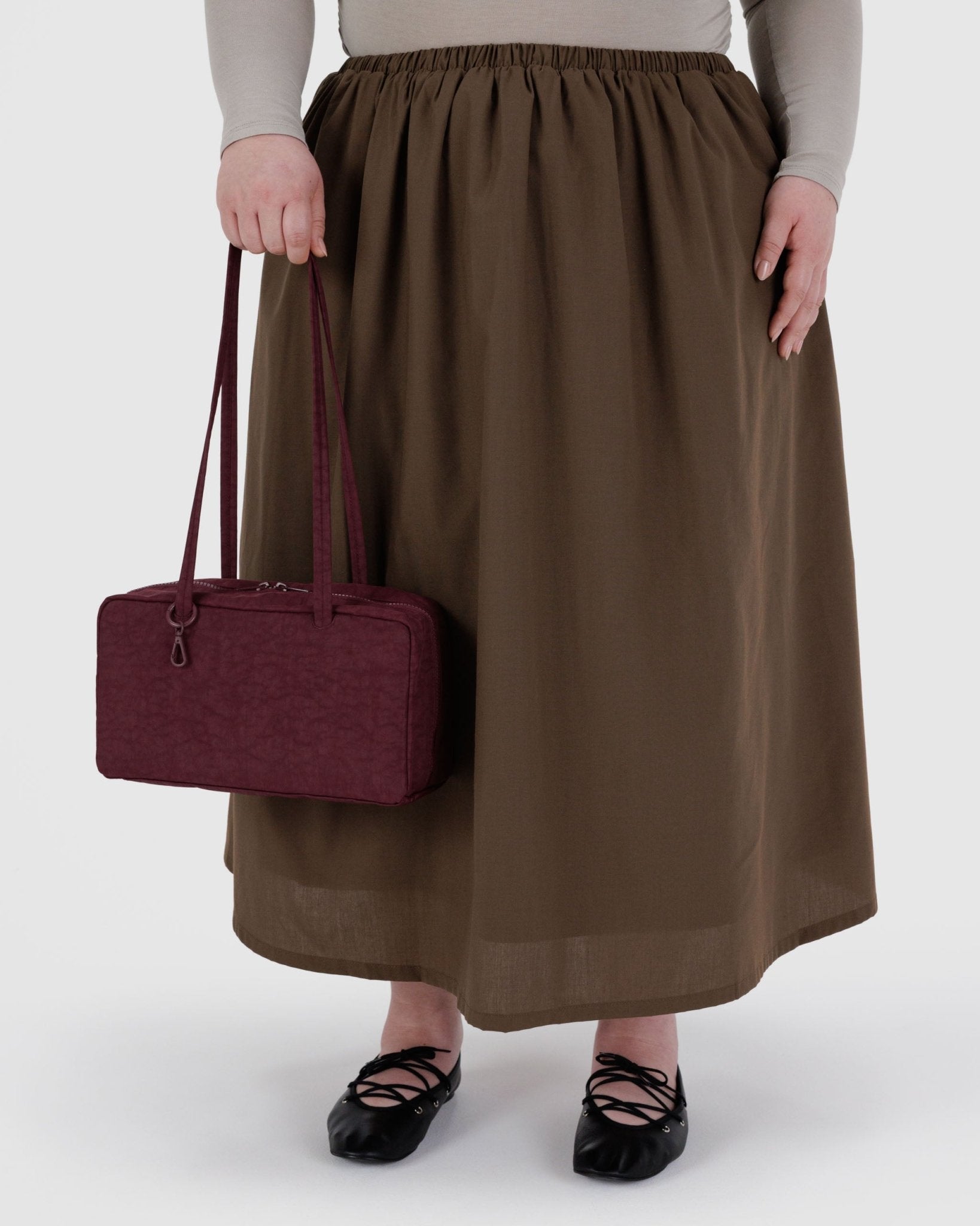 Person wearing a brown skirt holding a maroon handbag 