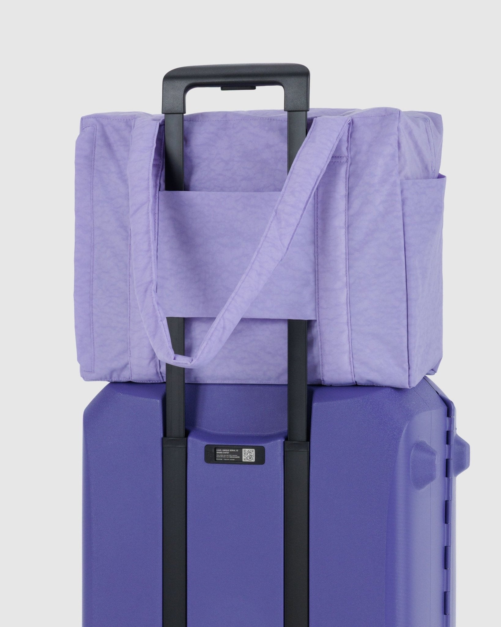 Small purple duffle bag with travel sleeve on handle of purple suitcase 