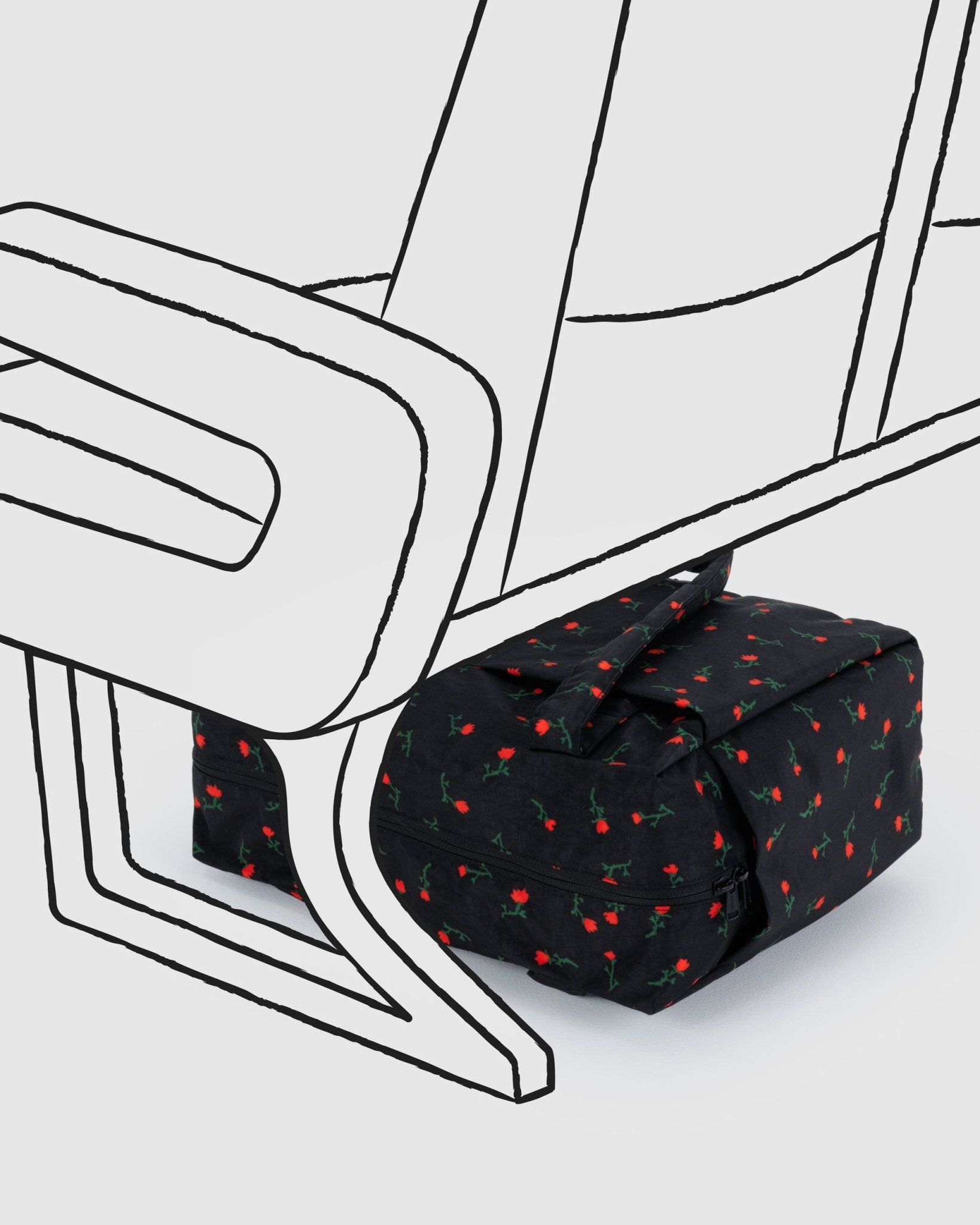 Small black duffel bag with red wildflowers pattern under an airline seat