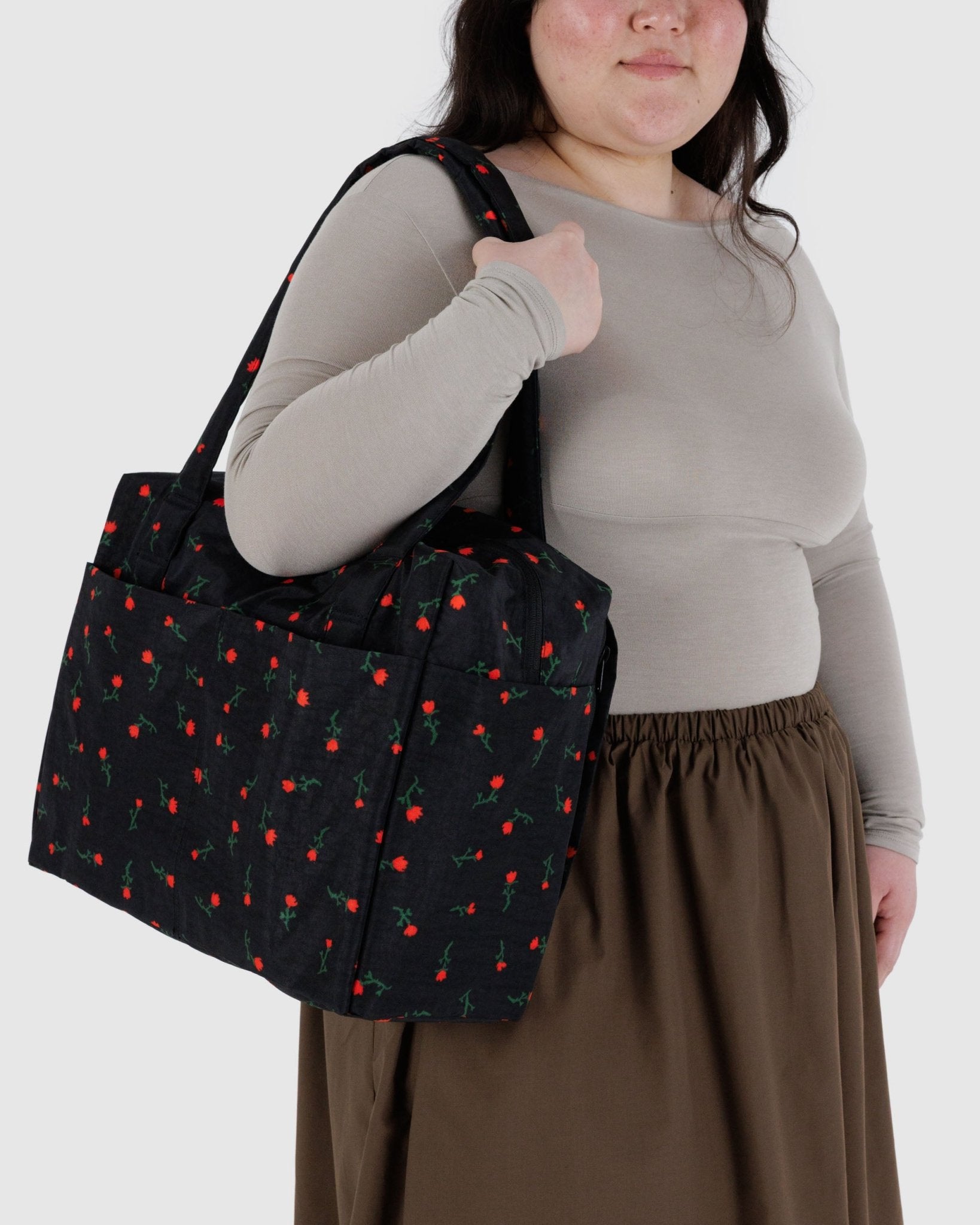 Person holding a small black duffle bag with red wildflower patterns on shoulder