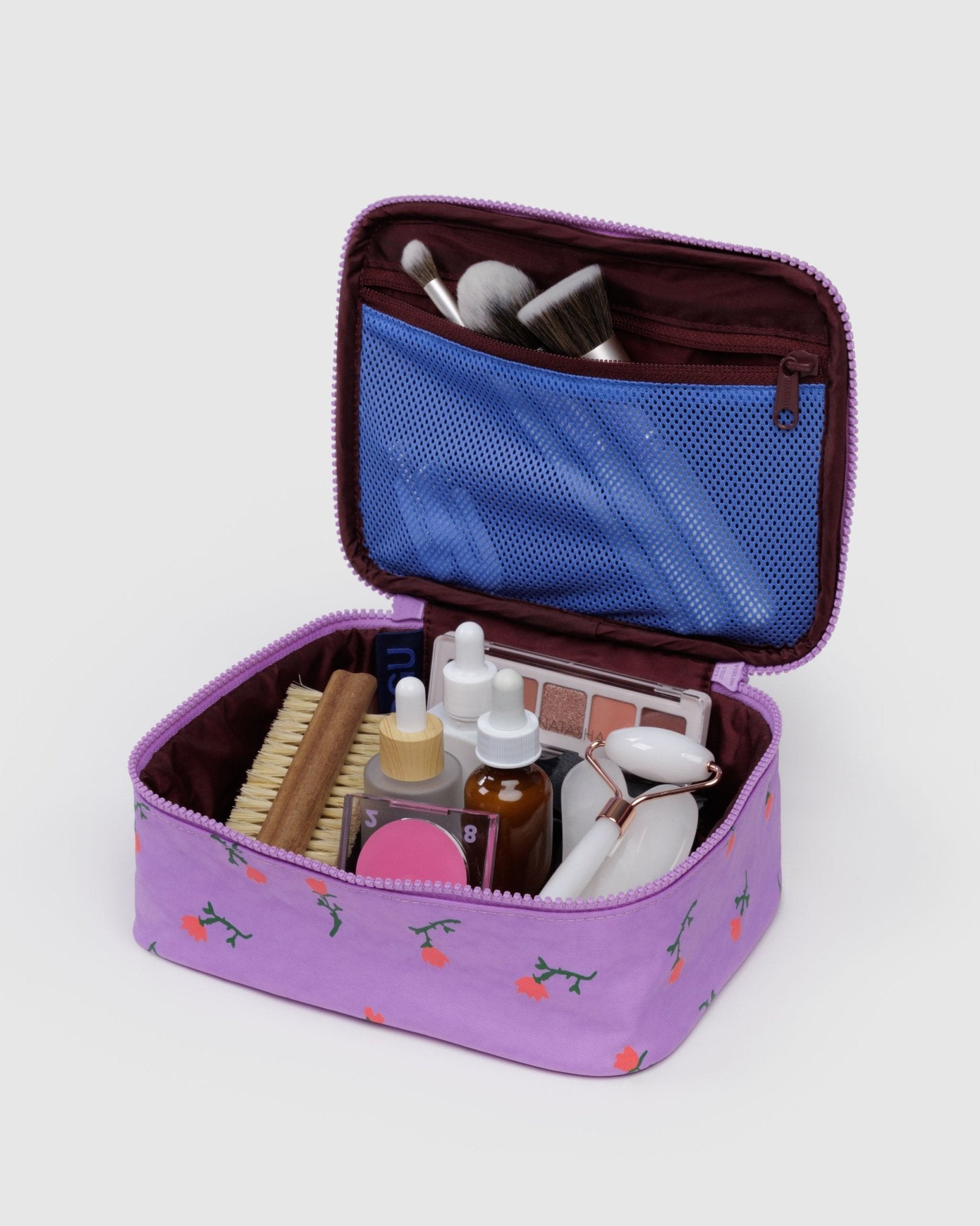 Small purple makeup bag with cosmetic items inside burgundy lined main compartment with blue mesh zip pocket in lid