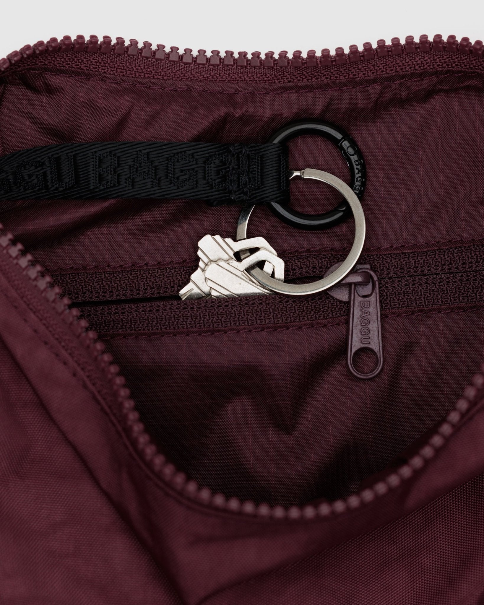 Close-up of a internal keychain with keys inside a zip pocket of a small maroon crescent bag