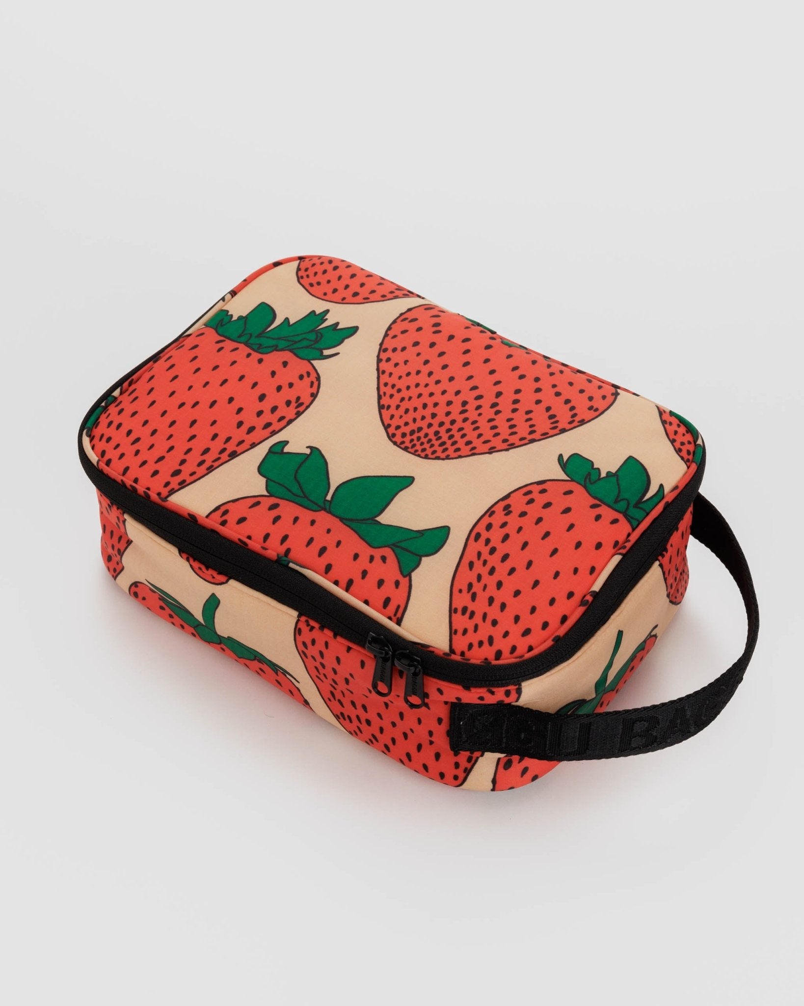 Baggu lunch box in light pink with a strawberry pattern and black webbed handle and zip fastening.