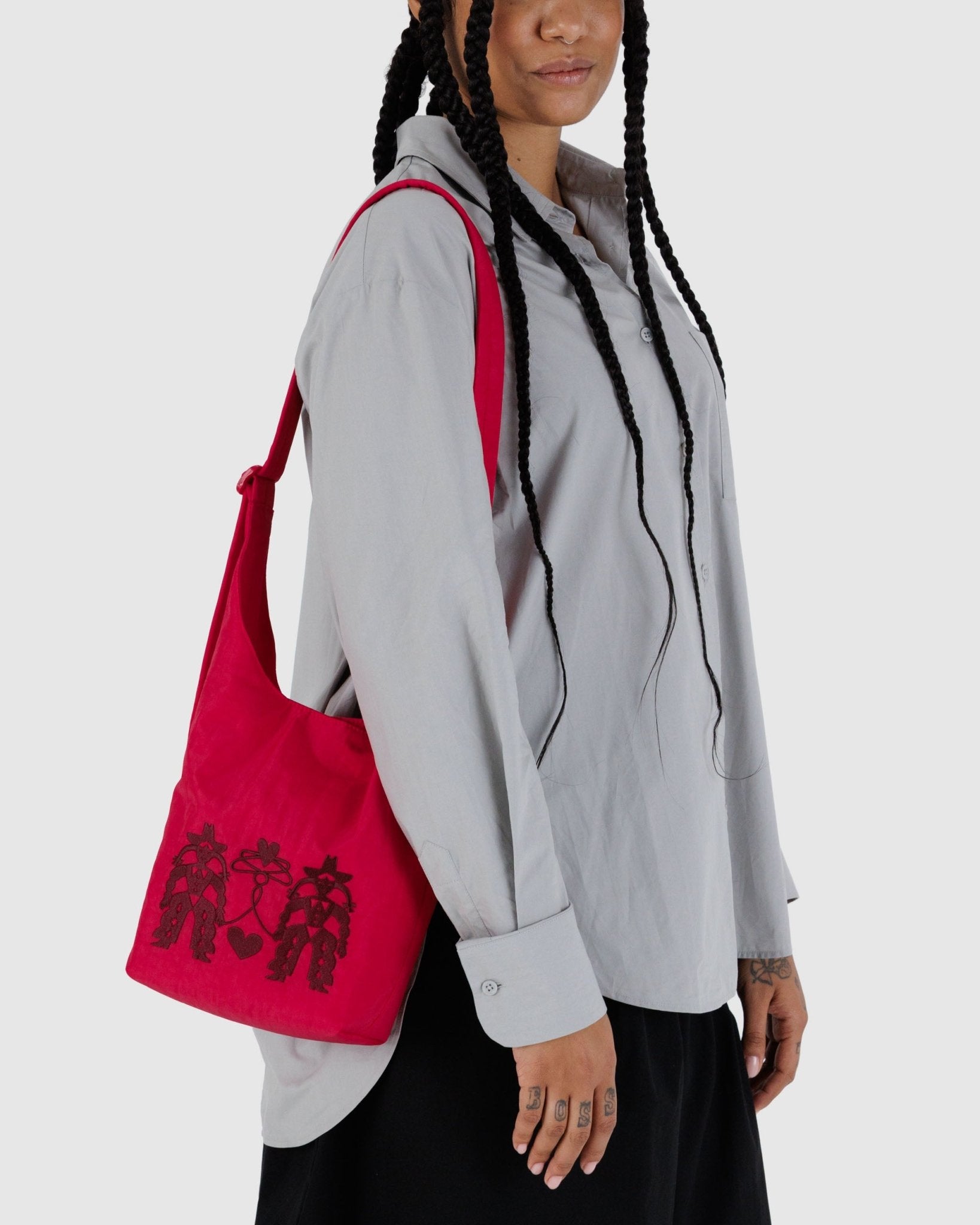 Person wearing a grey jacket with a red bag featuring black cowgirl and heart designs on a white background