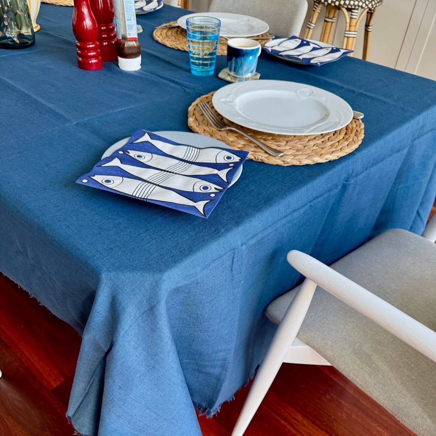 Dining table set with ocean blue tablecloth, plates, and cutlery.