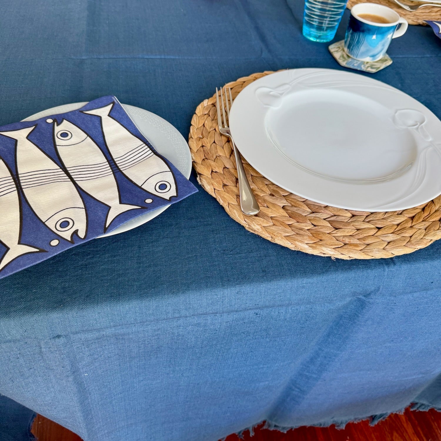 Table setting with a ocean blue tablecloth, ceramic plates, and woven placemats.