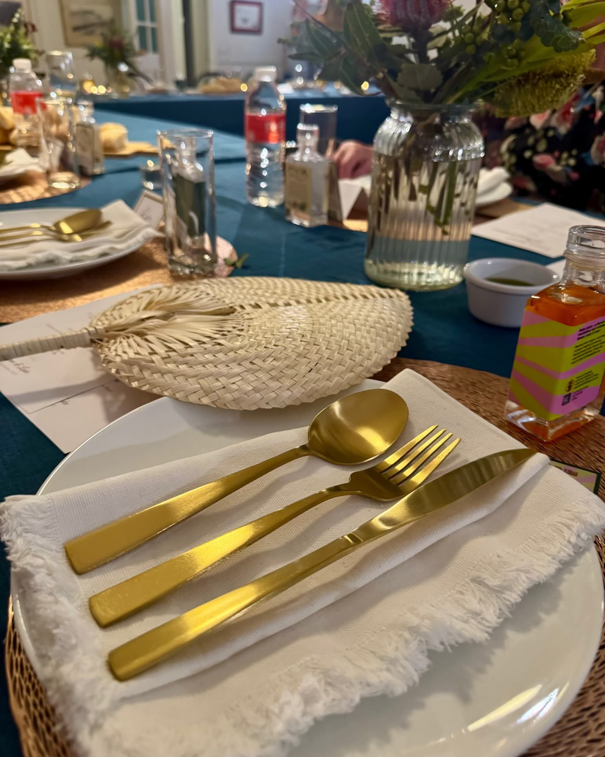 Gold cutlery on a white cotton frayed edge napkin set on a wedding table covered with teal rectangle tablecloth