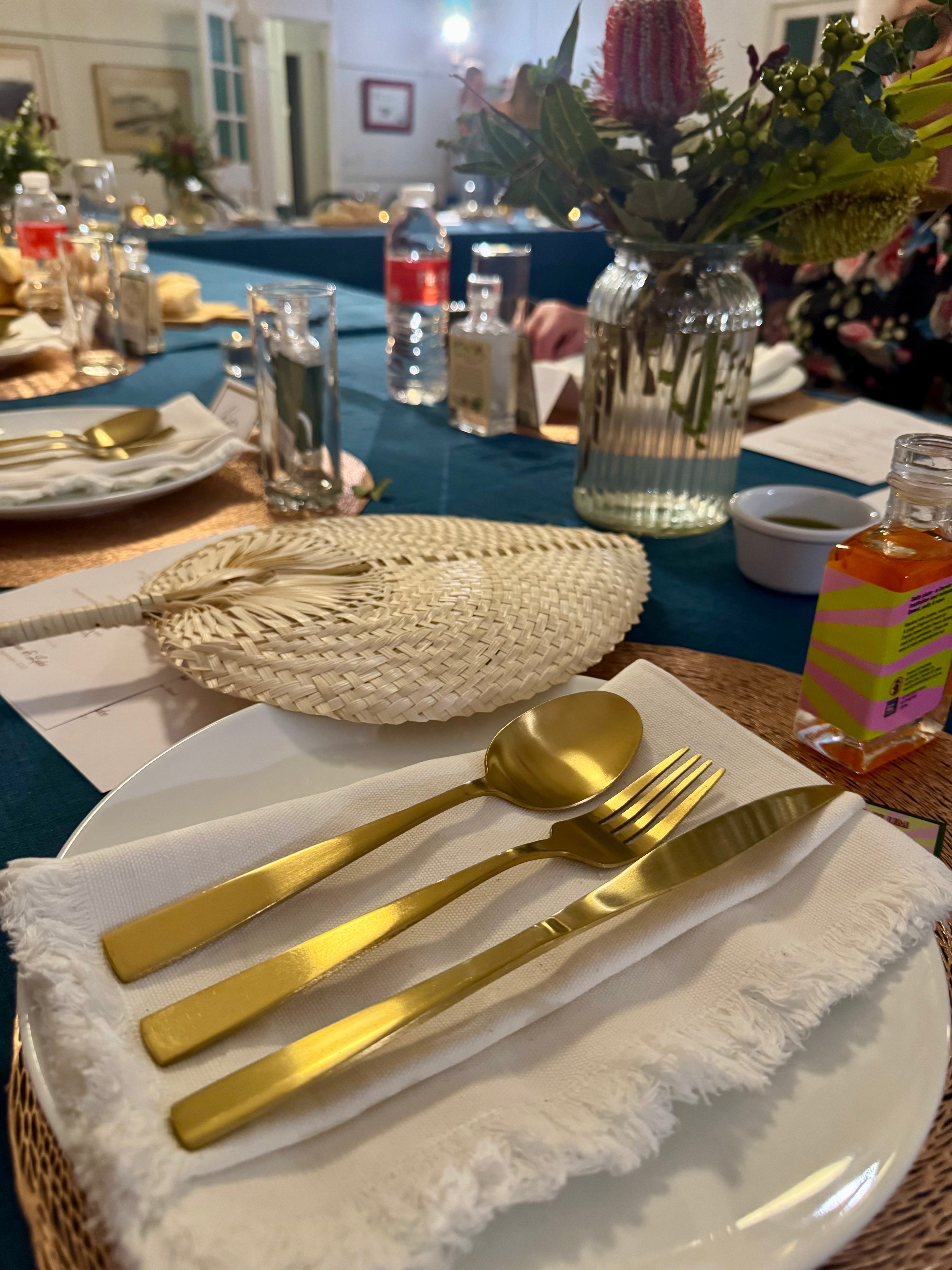 Gold cutlery on a white cotton frayed edge napkin set on a wedding table covered with teal rectangle tablecloth