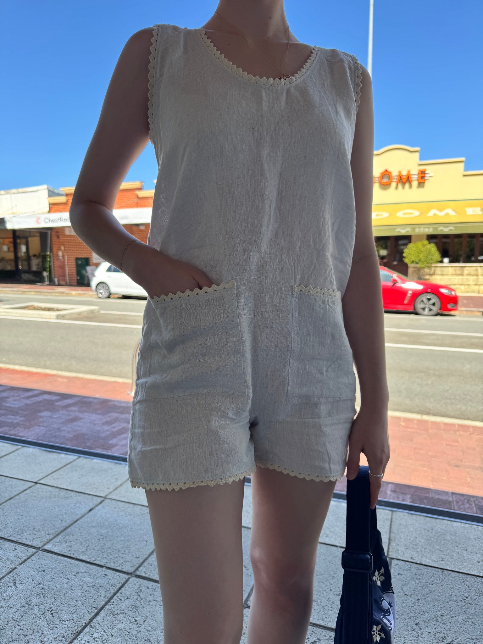 Close up of pocket and ric rac detail on light blue playsuit being worn by a woman holding a bag on a city street.