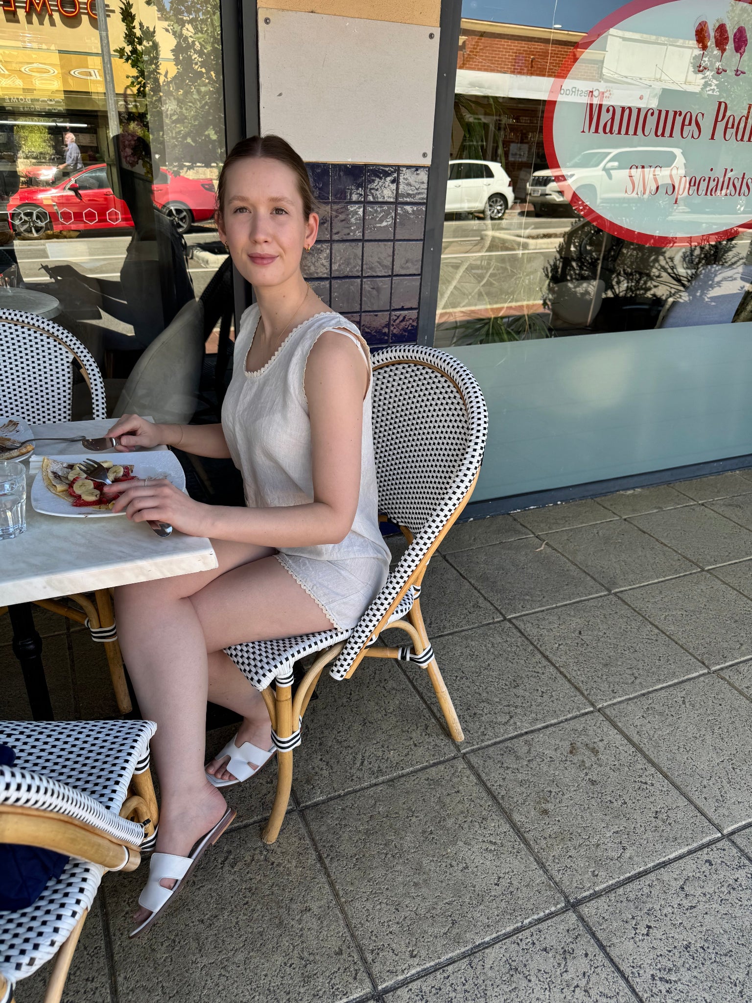 Woman in light blue playsuit with rac rac edges sitting at an outdoor cafe table with a menu in the background