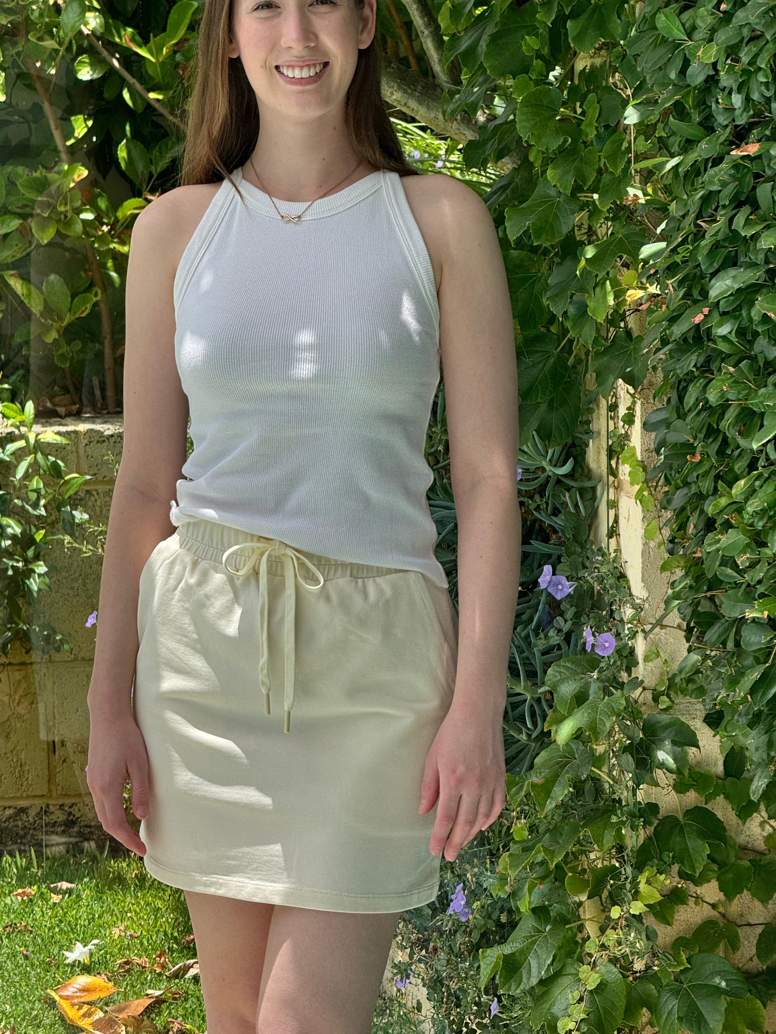 Woman wearing a white top and light yellow coloured skirt standing in a garden.