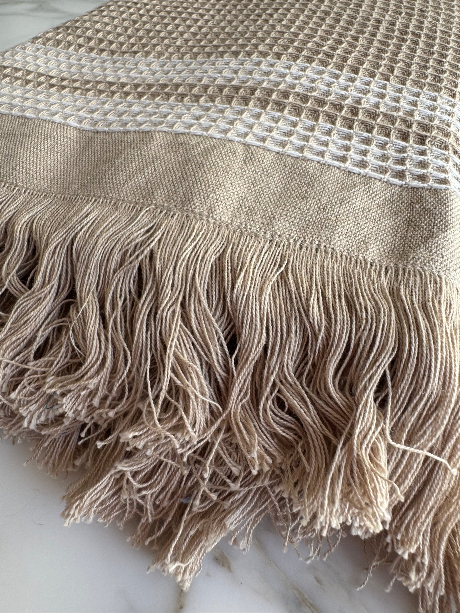 Close up of fringe on natural beach towel with a white stripe border.