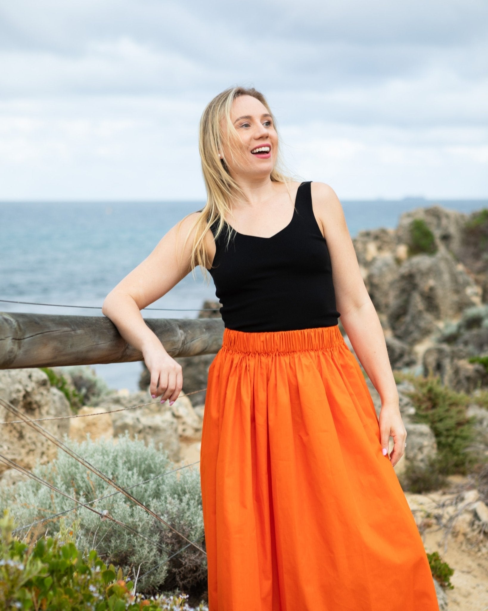 Woman wearing an orange gathered waist skirt and black top at beach path.
