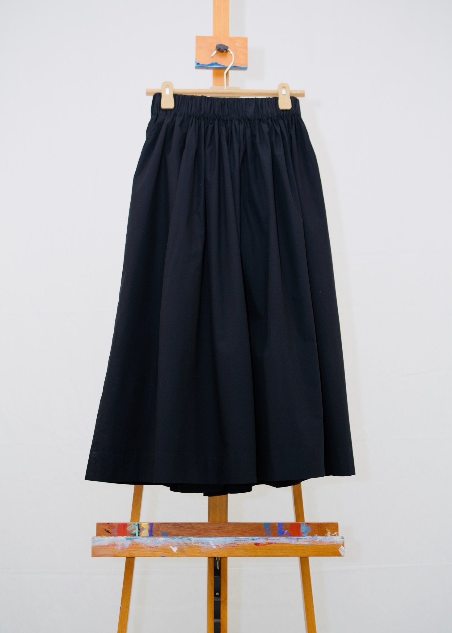 Jet black gathered waist cotton skirt hanging on a hanger on a painting easel - ANNIE.G