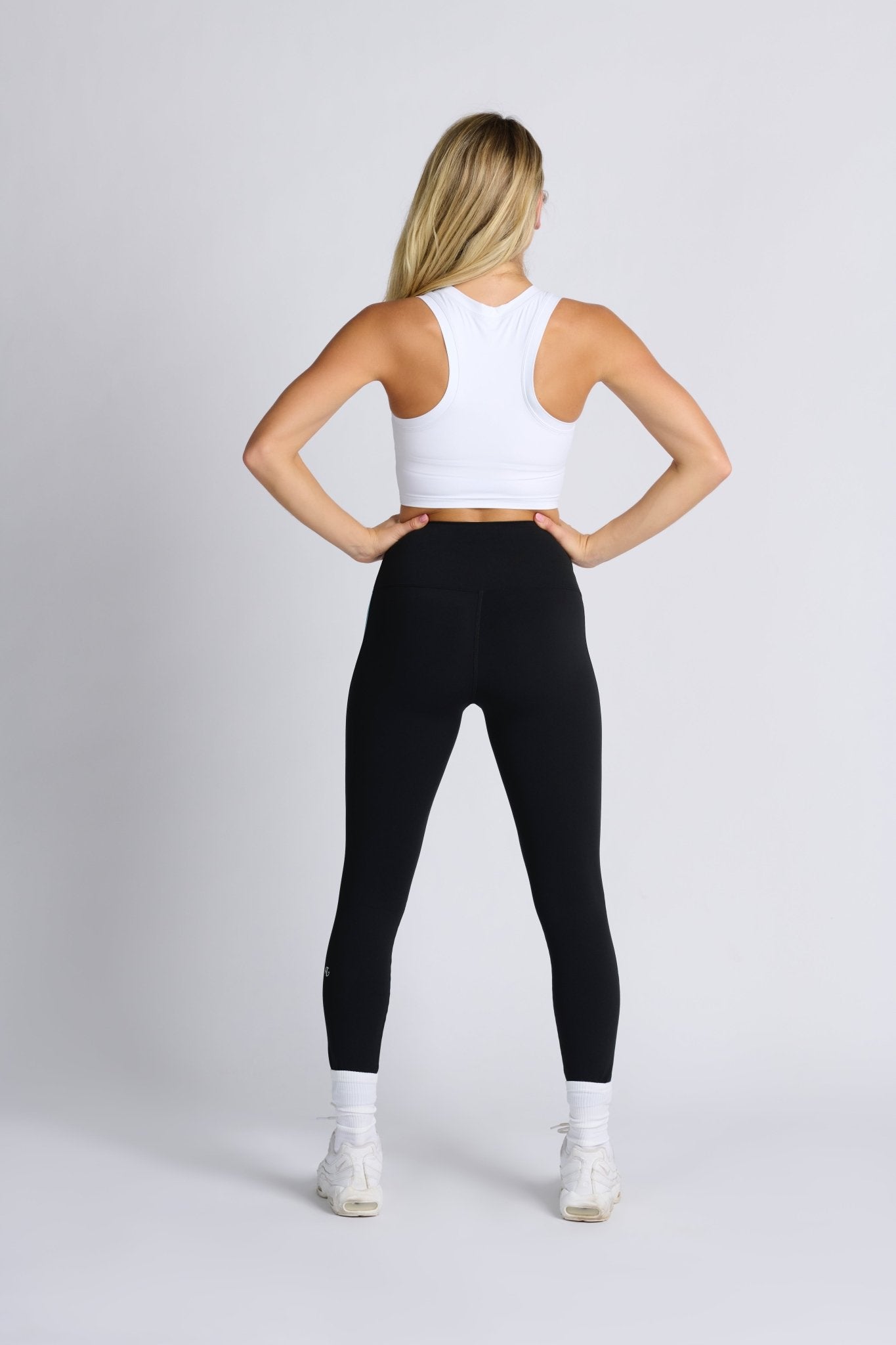 Back of a woman wearing Rayure High Waist Legging in Black with blue side stripe and racer back white crop top - ANNIE.G