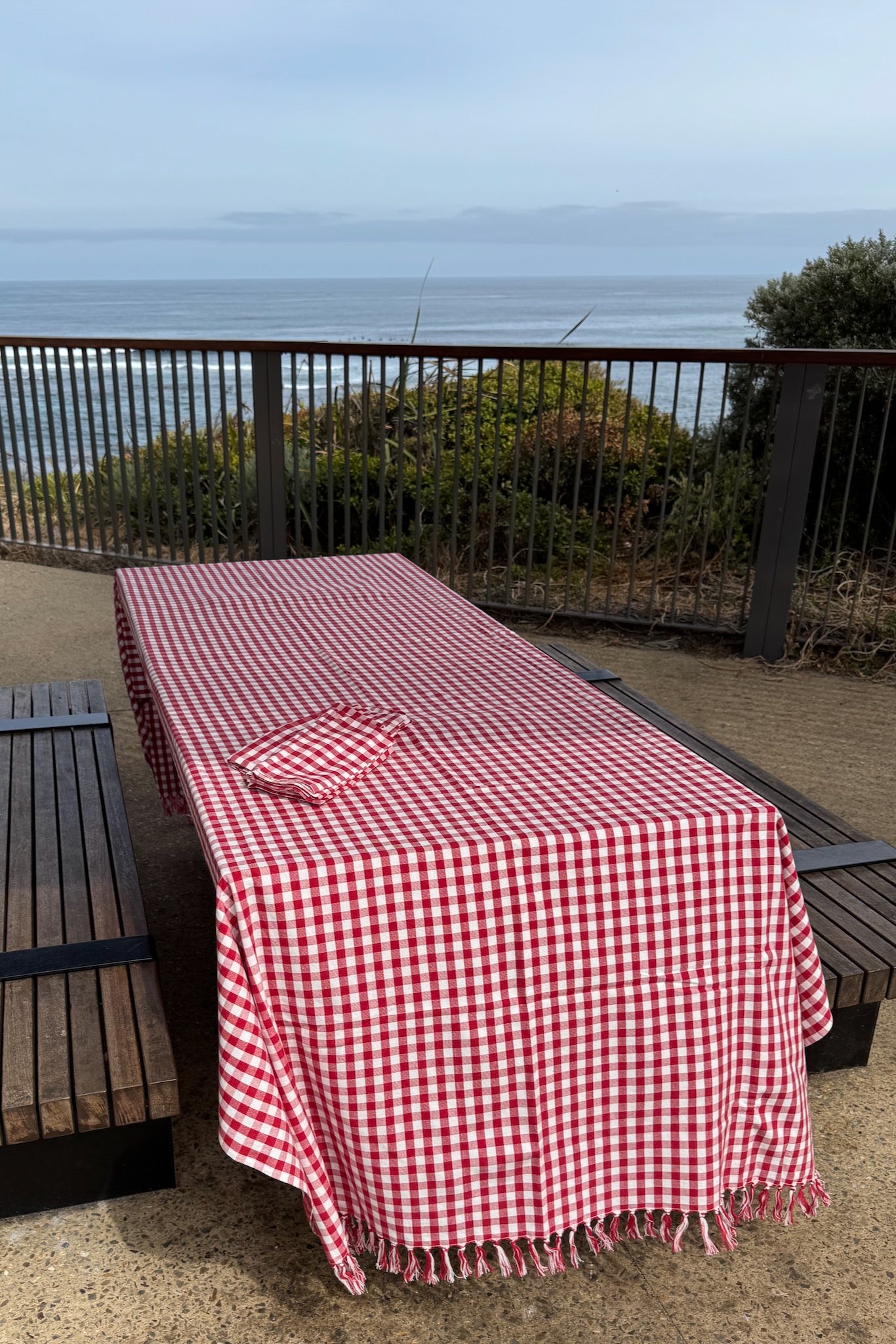 red-gingham-cotton-tablecloth-on-picnic-table-with-handknotted-edge-blowing-in-wind