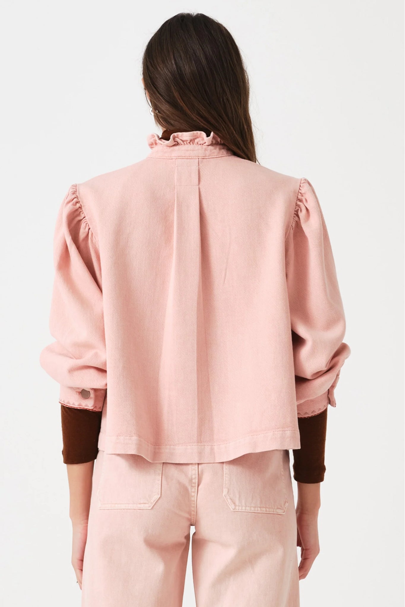 Back of a woman wearing a pink jacket and jeans with pockets outfit with sleeves of maroon top showing