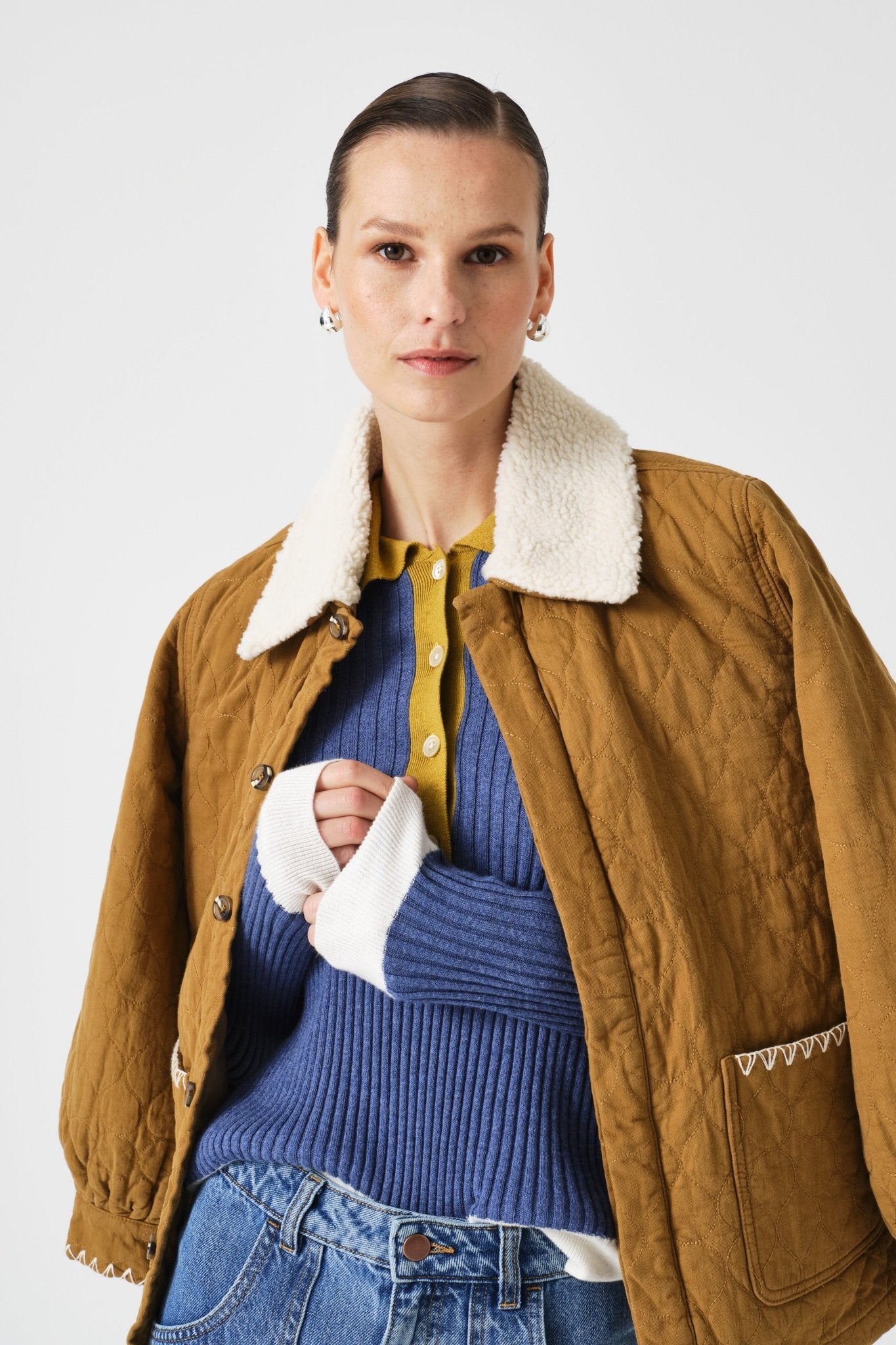 Woman wearing a brown jacket with a white collar, blue sweater, and jeans