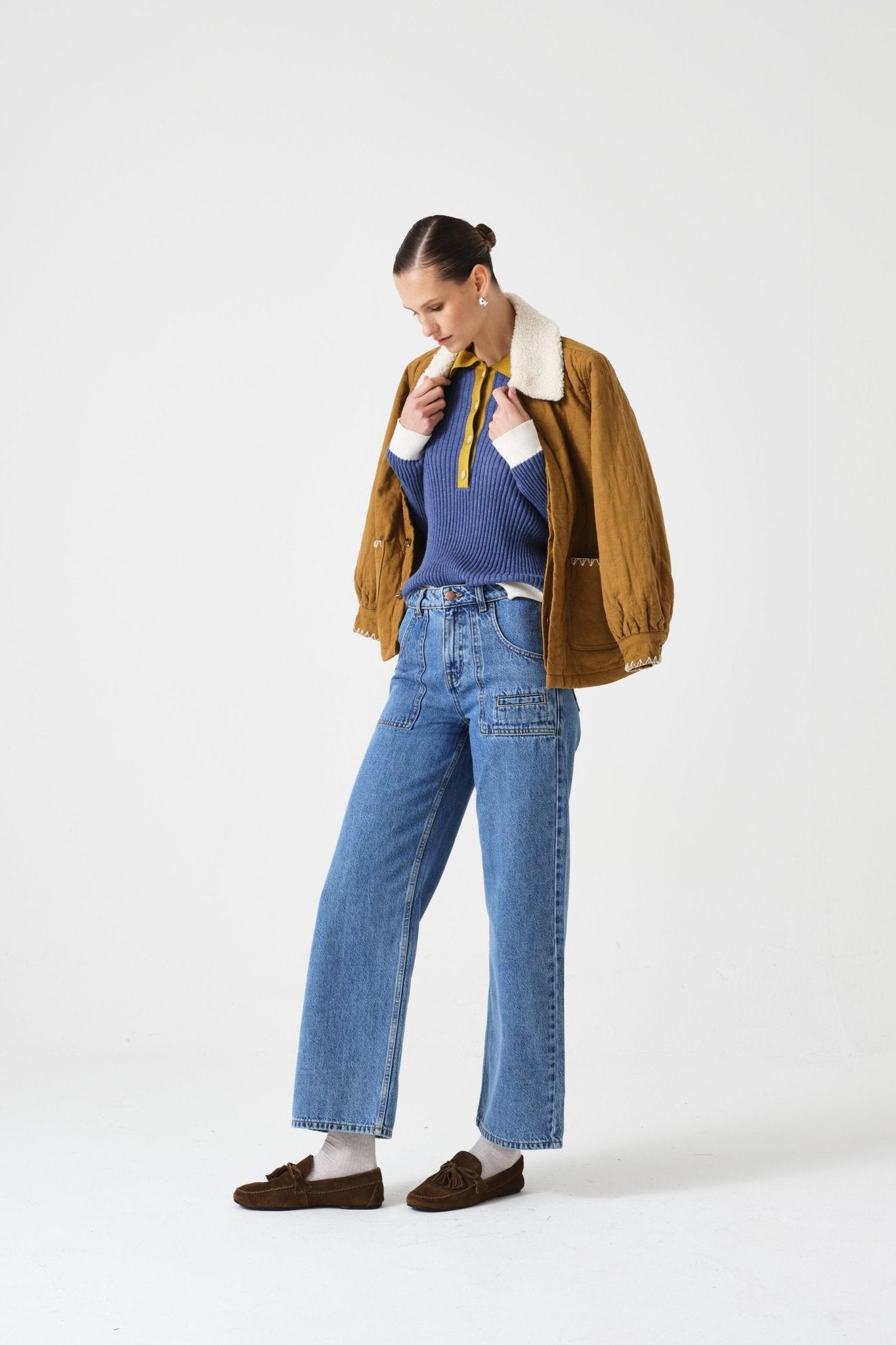 Person wearing a blue top, brown jacket over shoulders, and jeans