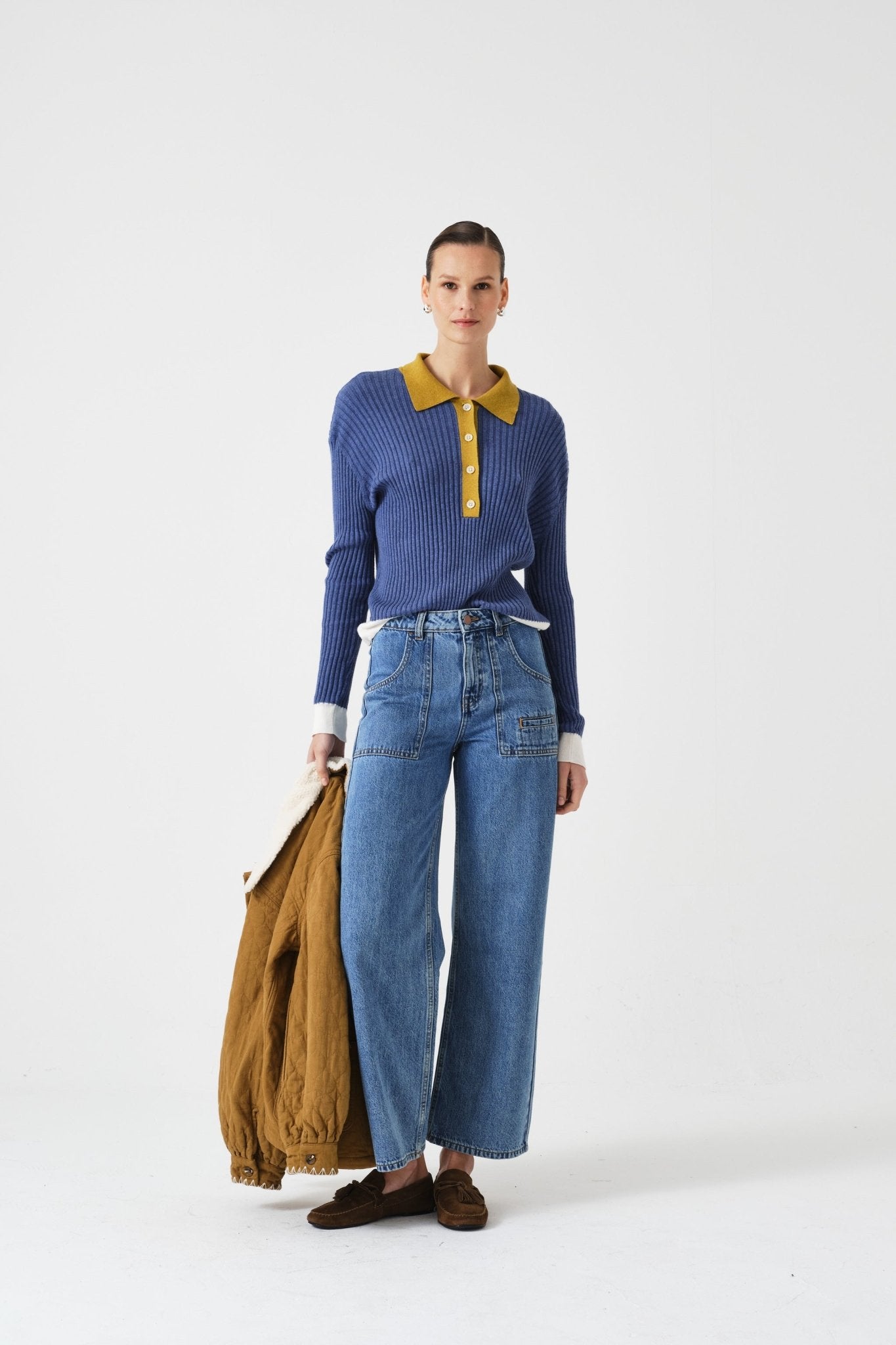 Person wearing a blue sweater with yellow collar and blue jeans, holding a brown jacket