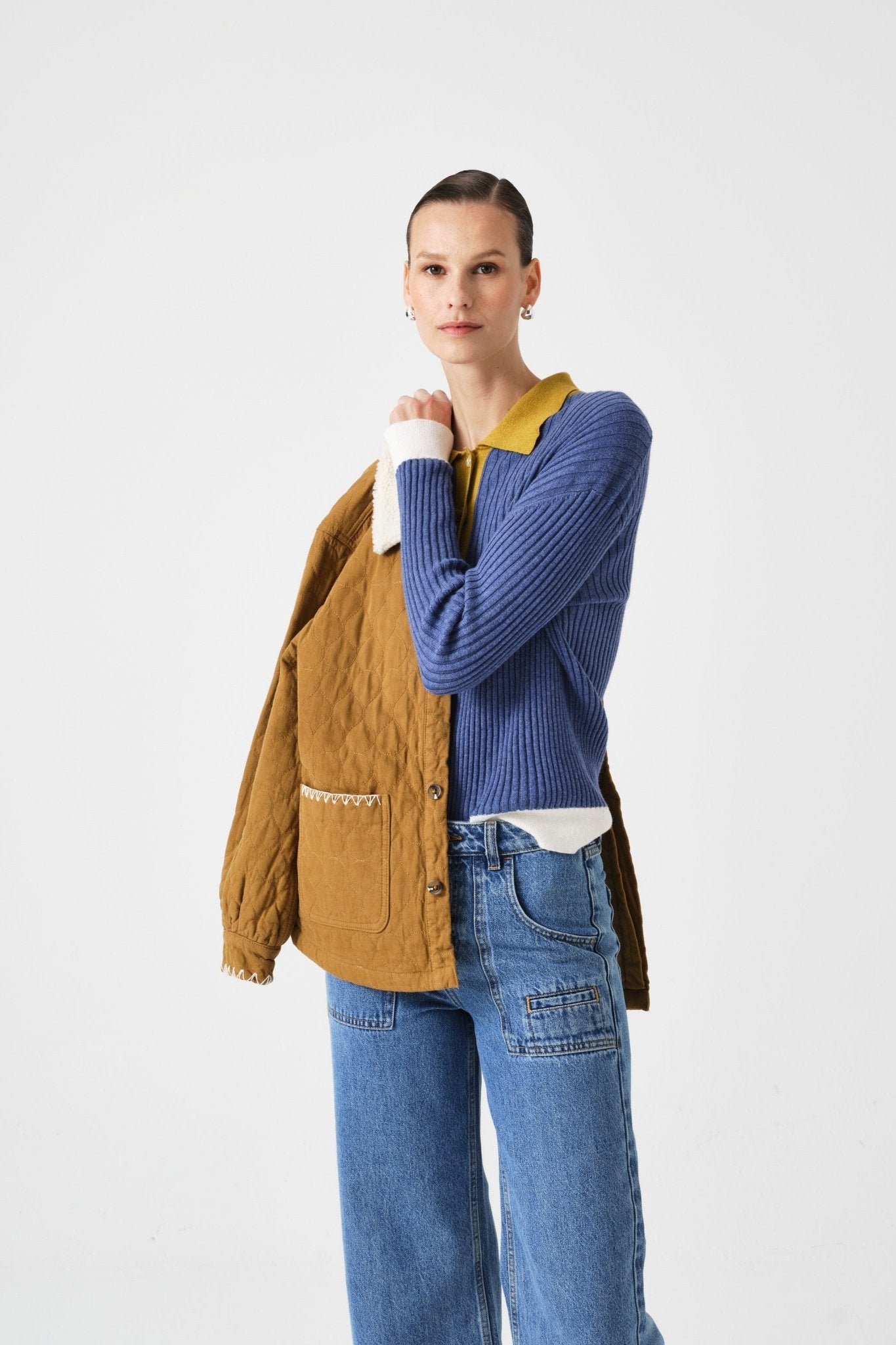 Woman putting a brown jacket on her arm wearing a blue sweater and blue jeans