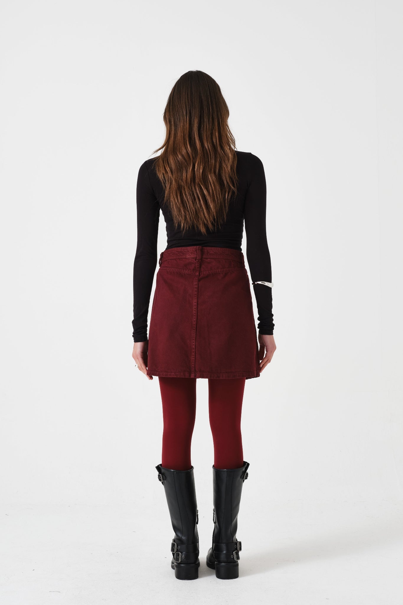 Person wearing a black top, mulberry mini skirt, and black boots