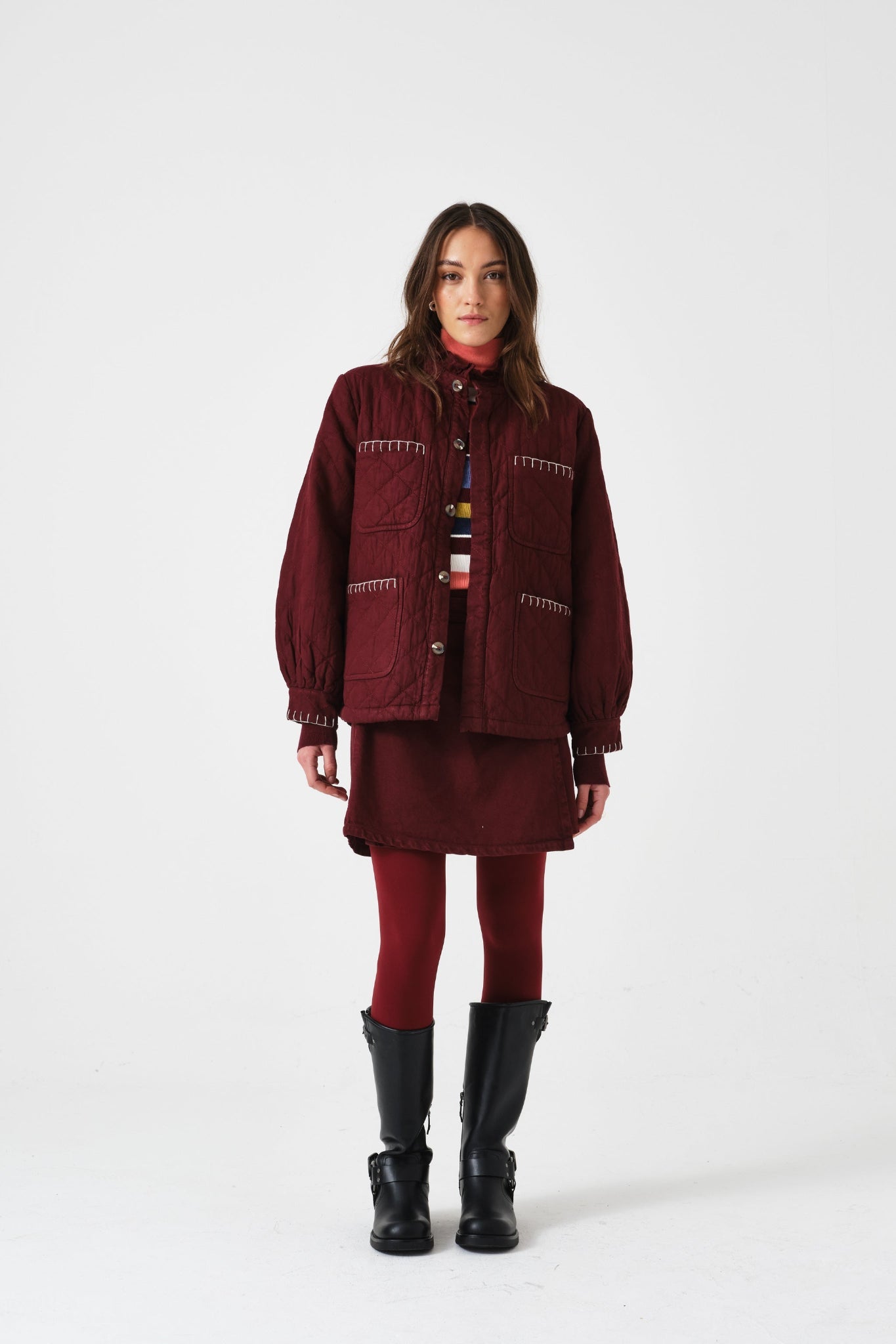 Woman wearing a burgundy outfit with a quilted jacket, mini skirt, and boots.