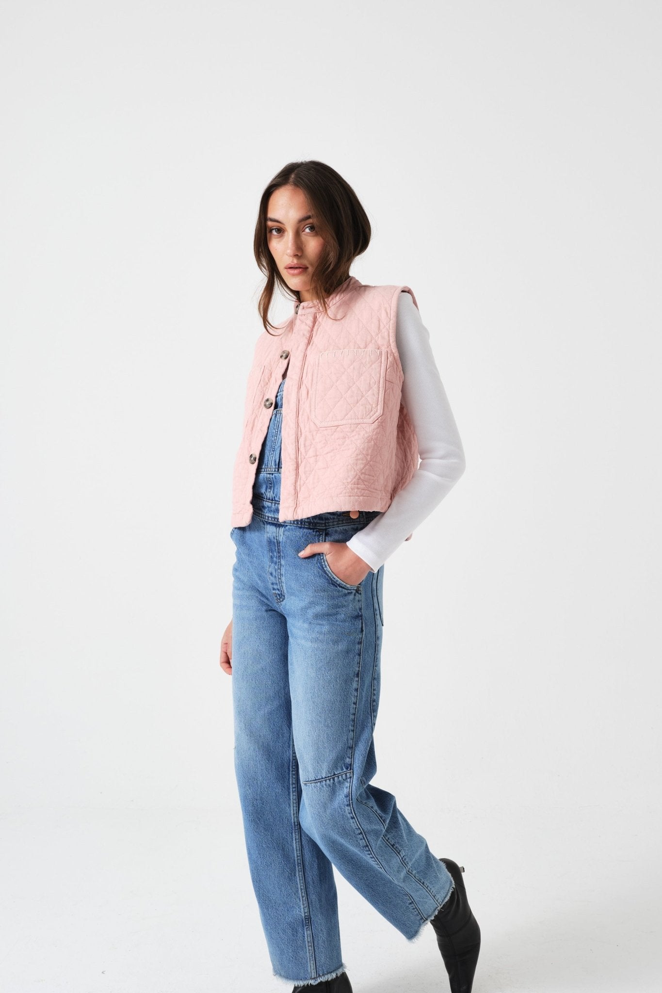 Woman wearing a pink quilted vest with buttons over a white shirt with blue jeans