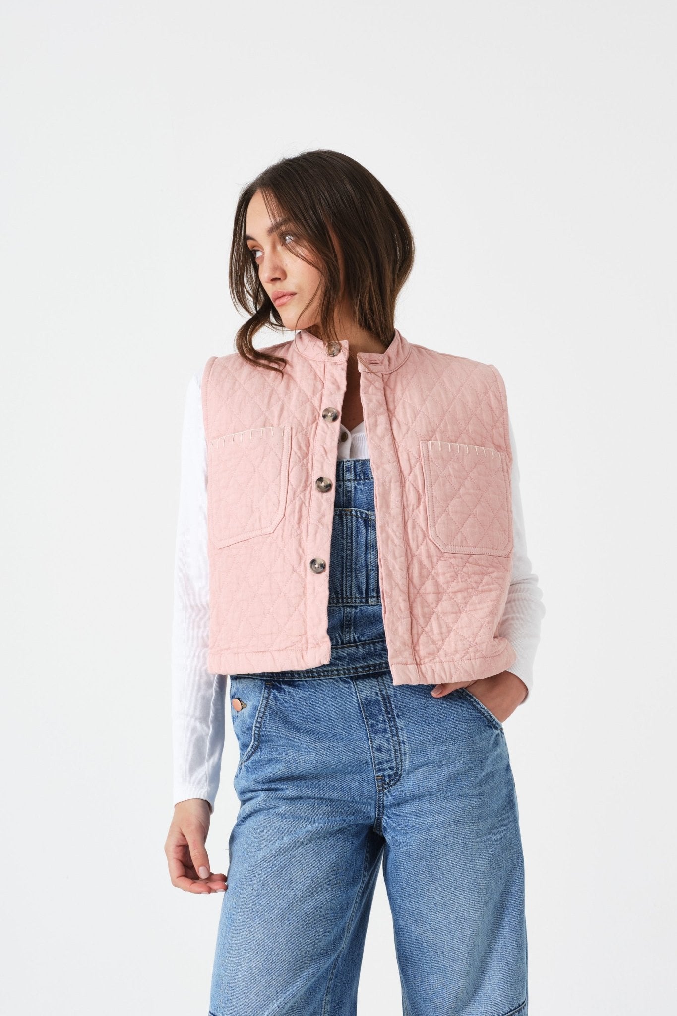 Woman wearing a sleeveless pink quilted vest with patch pockets and buttons over a white shirt and blue jeans
