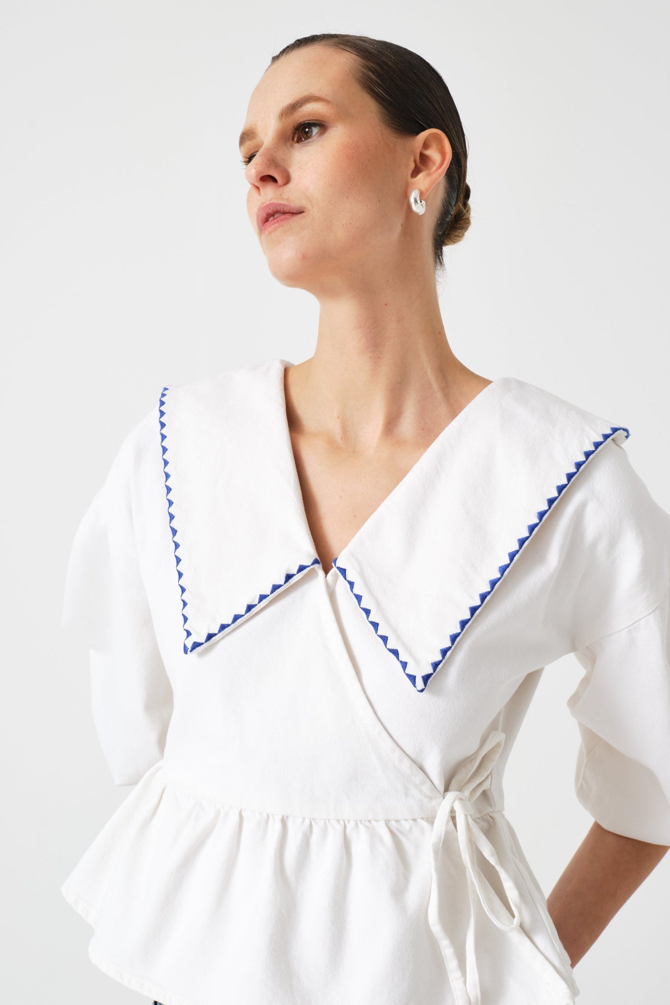 Woman wearing a white wrap blouse with blue embroidery on collar and tie at side