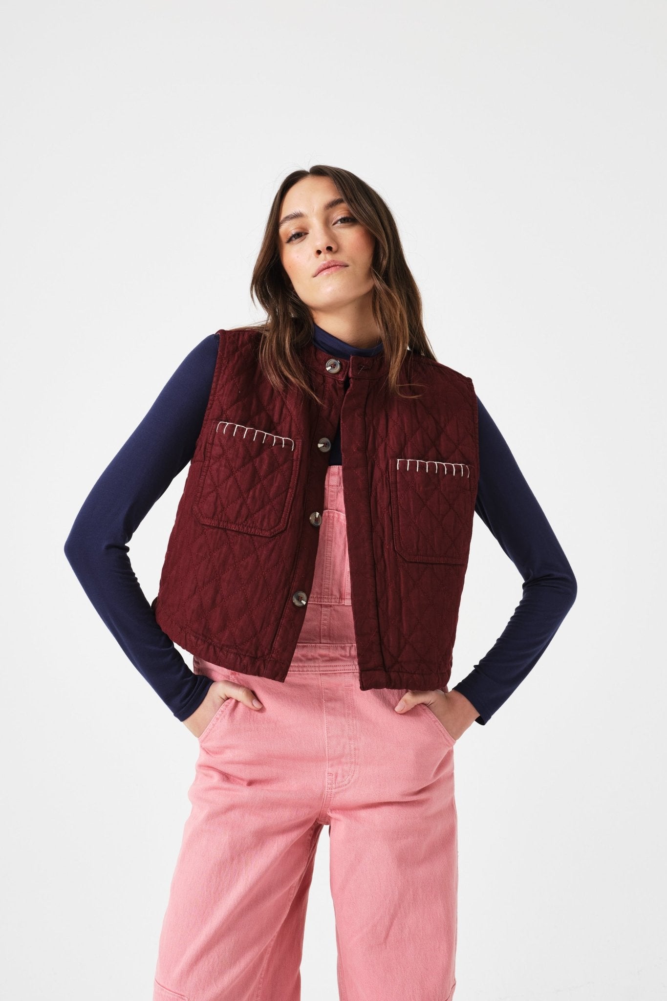Woman wearing a mulberry vest buttons open over a navy long-sleeve shirt with pink jeans