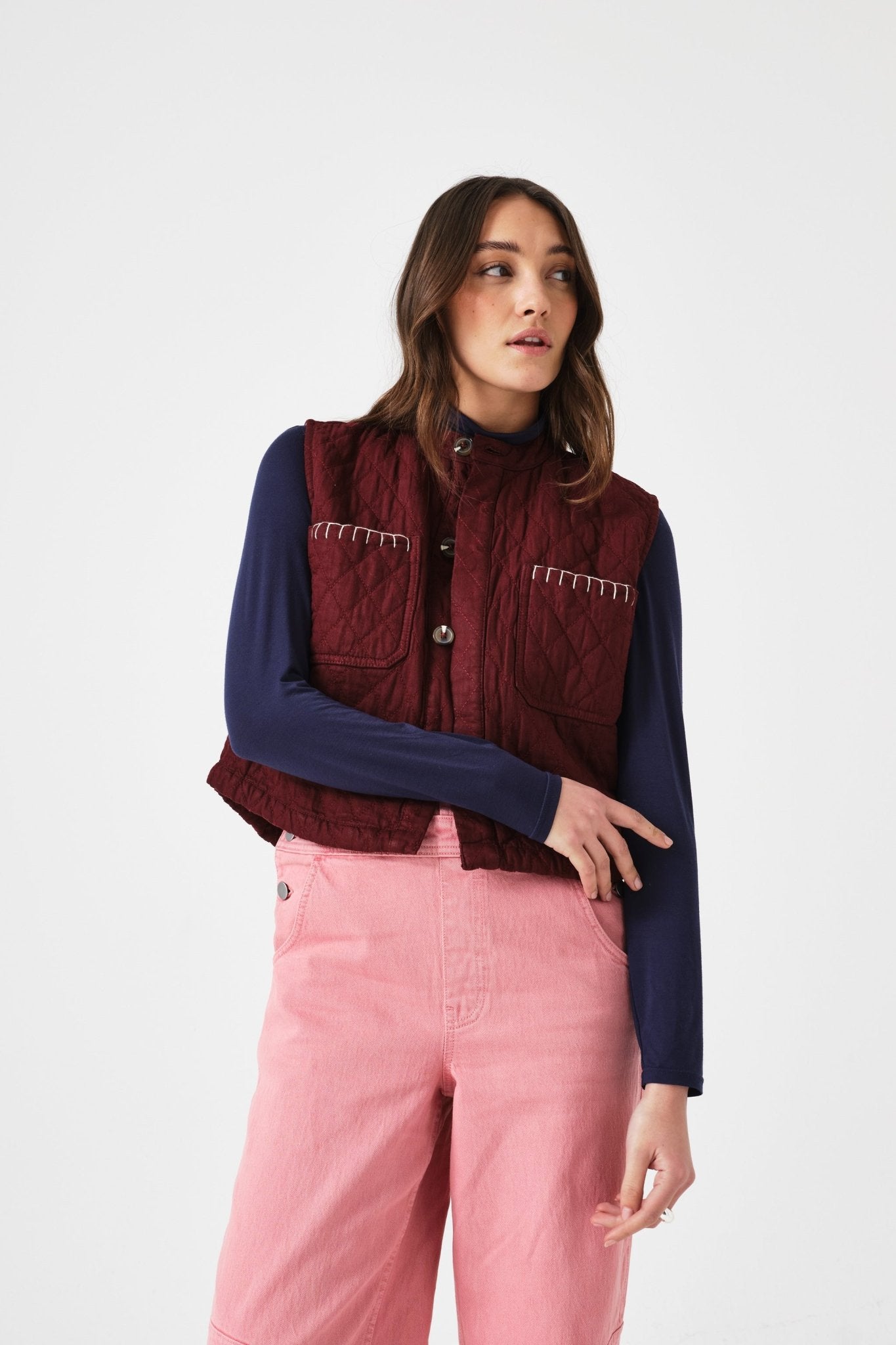 Woman wearing a mulberry vest over a blue shirt with arm across vest and pink pants